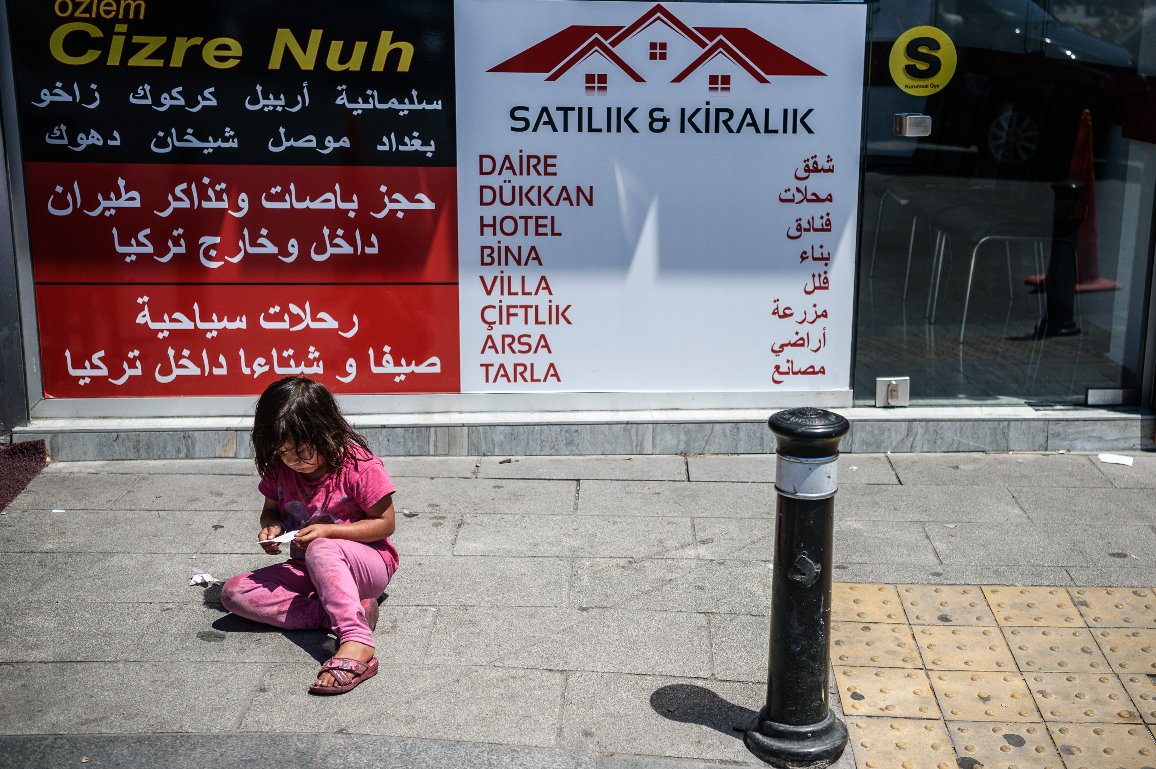 A Syrian girl stays next to a travel agency with Arabic letters on its window on July 4 ,2016 in Fatih neighbourhood in Istanbul. Receptionist, waiter, hairdresser, pastry-seller : these are the jobs of the young Syrians who abandoned their dreams in Damascus to start from scratch in Istanbul. In Fatih, a densely-packed neighbourhood that serves as a hub for Arabs living in Turkey's biggest city, the signs of home are everywhere. / AFP PHOTO / OZAN KOSE