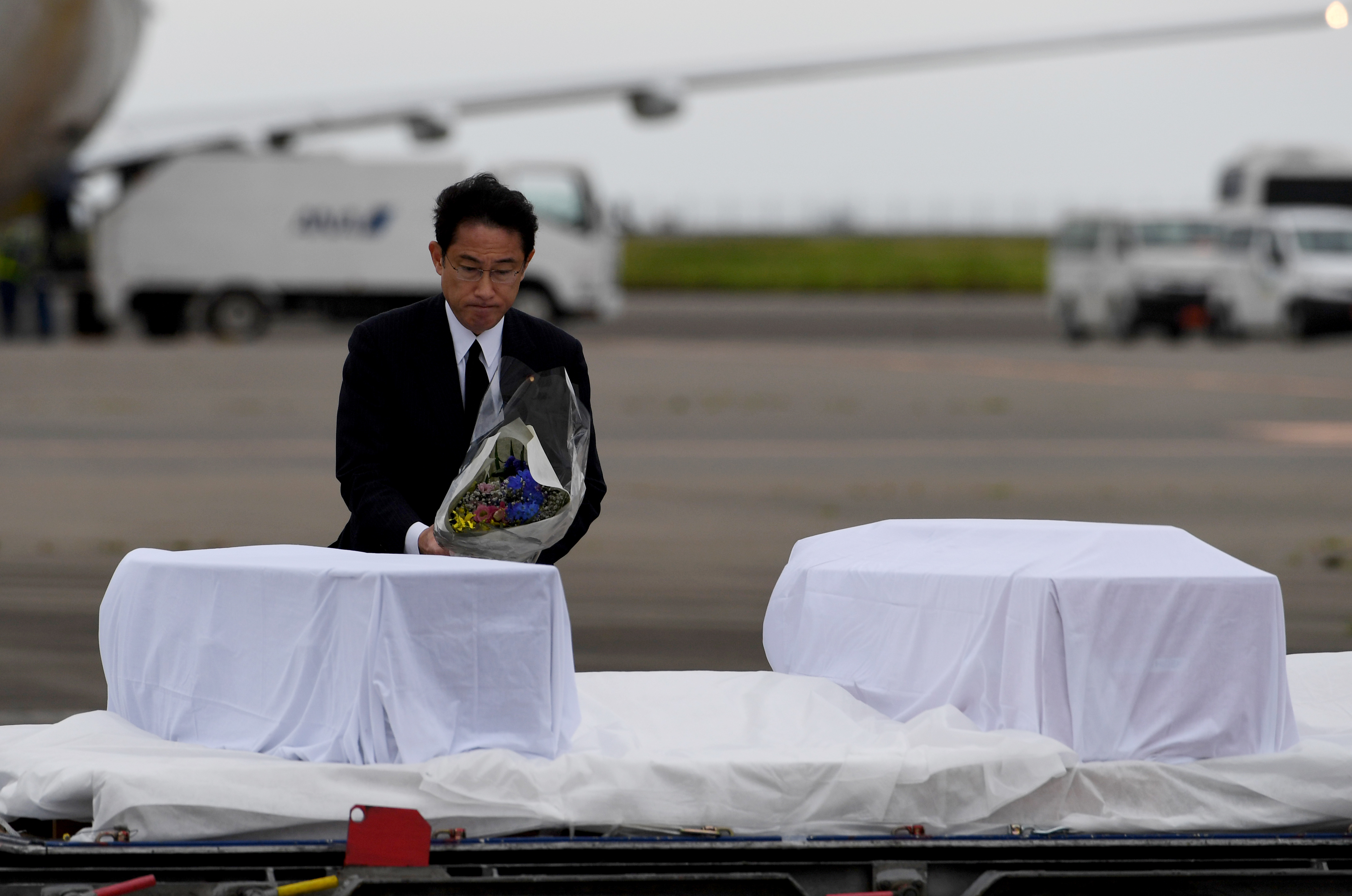 Japanese Foreign Minister Fumio Kishida places a bouquet of flowers among the coffins of Japanese victims upon their arrival at Tokyo International Airport at Haneda on July 5, 2016 from Dhaka following a siege at a Bangladesh café. Hostage-takers on July 1 killed 20, including seven Japanese nationals, all of whom were engaged in development projects in Bangladesh with the government-run Japan International Cooperation Agency (JICA). / AFP PHOTO / TOSHIFUMI KITAMURA