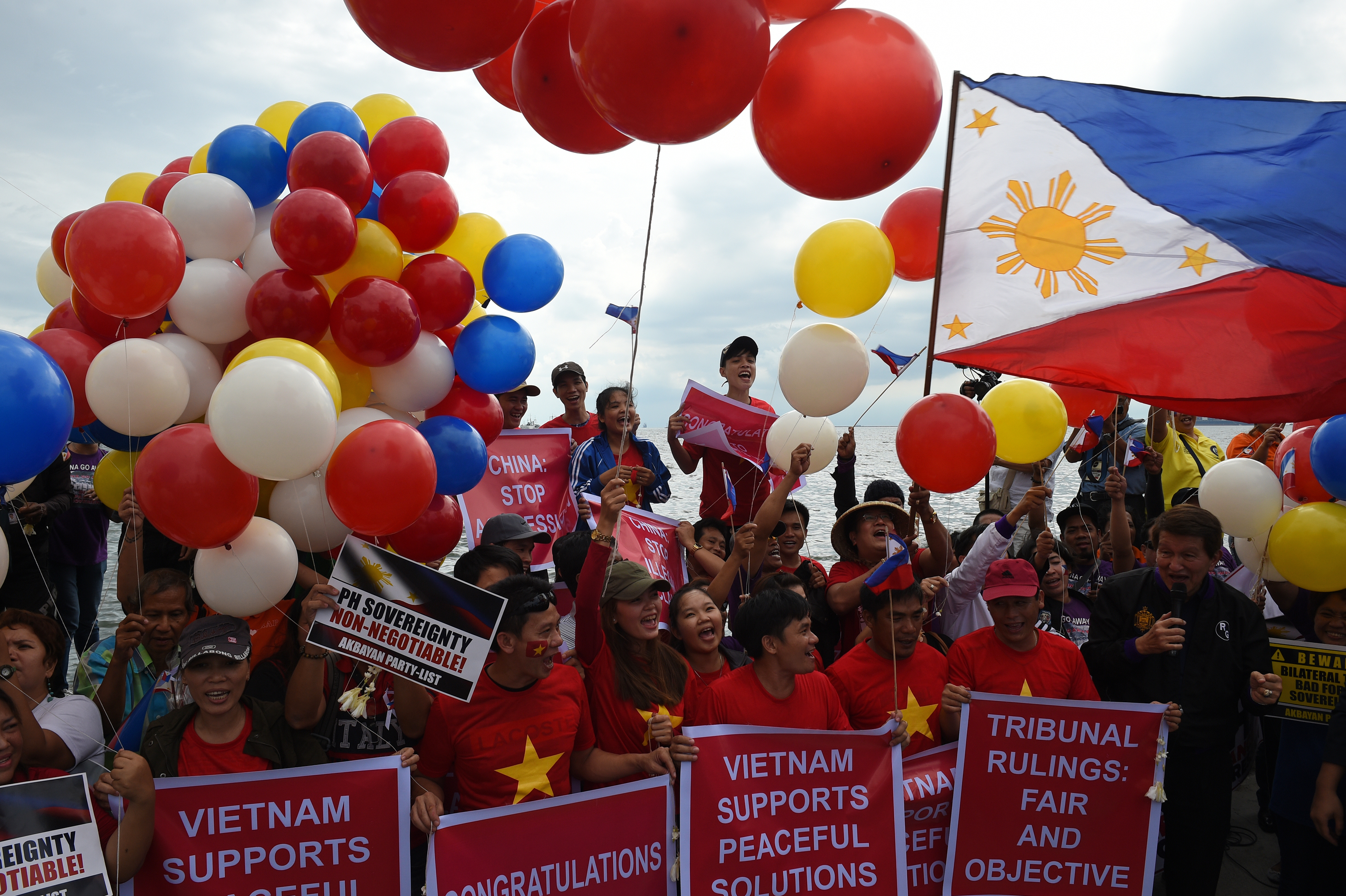 Filipino activists and Vietnamese nationals release balloons and wave Philippine flags as they anticipate a favourable decision from a UN tribunal ruling on the legality of China's claims to an area of the South China sea contested by the Philippines, during a demonstration along the bay walk in Roxas Boulevard in Manila on July 12, 2016. The Philippines welcomes a ruling by a UN-backed tribunal on July 12 that declares China has no "historic rights" in the South China Sea, Foreign Secretary Perfecto Yasay said, as he urged restraint.  / AFP PHOTO / TED ALJIBE