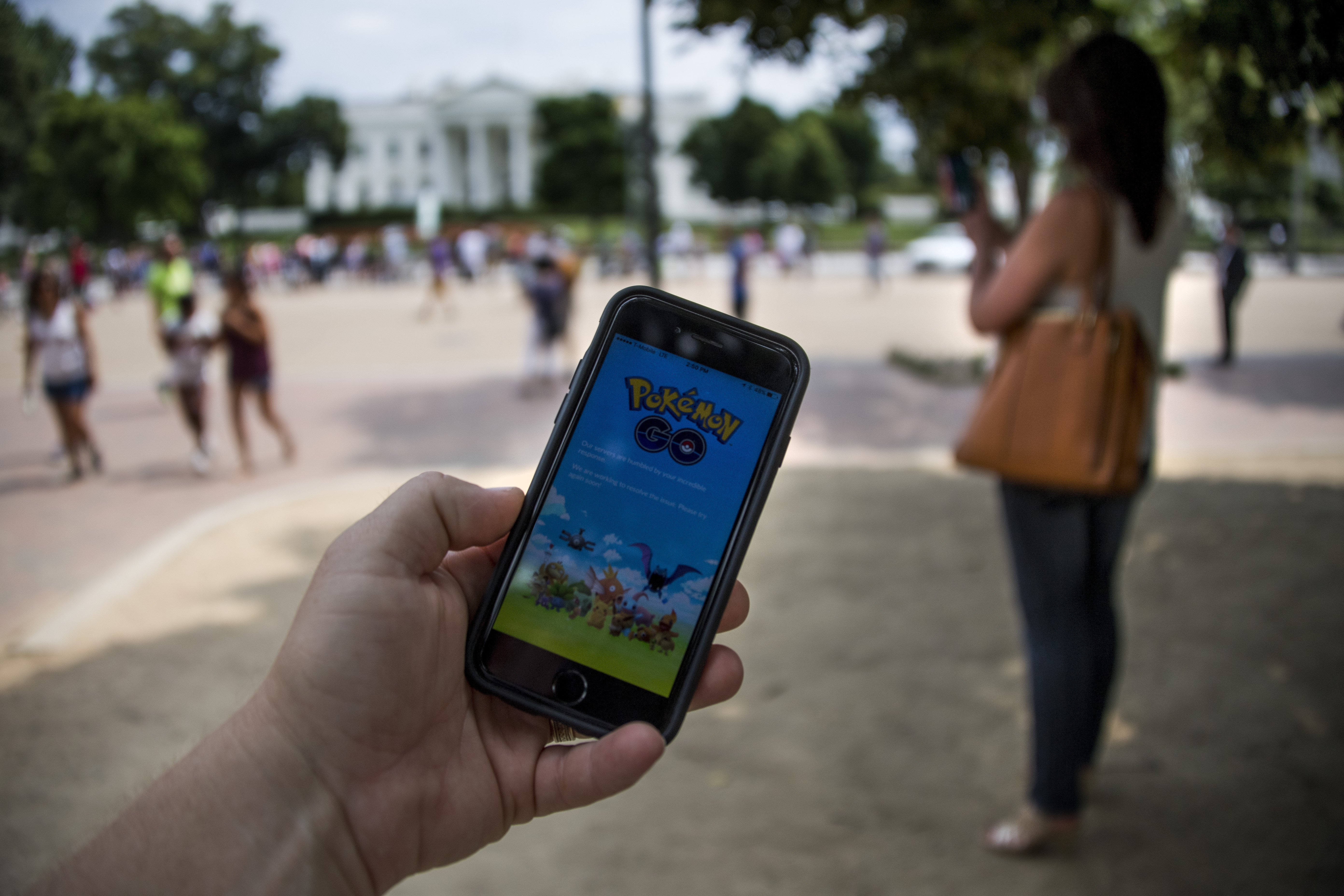 A man holds up his cell phone with a screen shot of the Pokemon Go game as a woman searches on her cell phone for a Pokemon in front of the White House in Washington, DC, July 12, 2016. Pokémon Go mania is sweeping the US as players armed with smartphones hunt streets, parks, rivers and elsewhere to capture monsters and gather supplies in the hit game. The free application based on a Nintendo title that debuted 20 years ago has been adapted to the mobile internet Age by Niantic Labs, a company spun out of Google last year after breaking ground with an "Ingress" game that merged mapping capabilities with play. As of July 11, 2016 Pokémon Go had been downloaded millions of times, jumping topping rankings at official online shops for applications tailored for smartphones powered by Apple or Google-backed Android software.  / AFP PHOTO / JIM WATSON