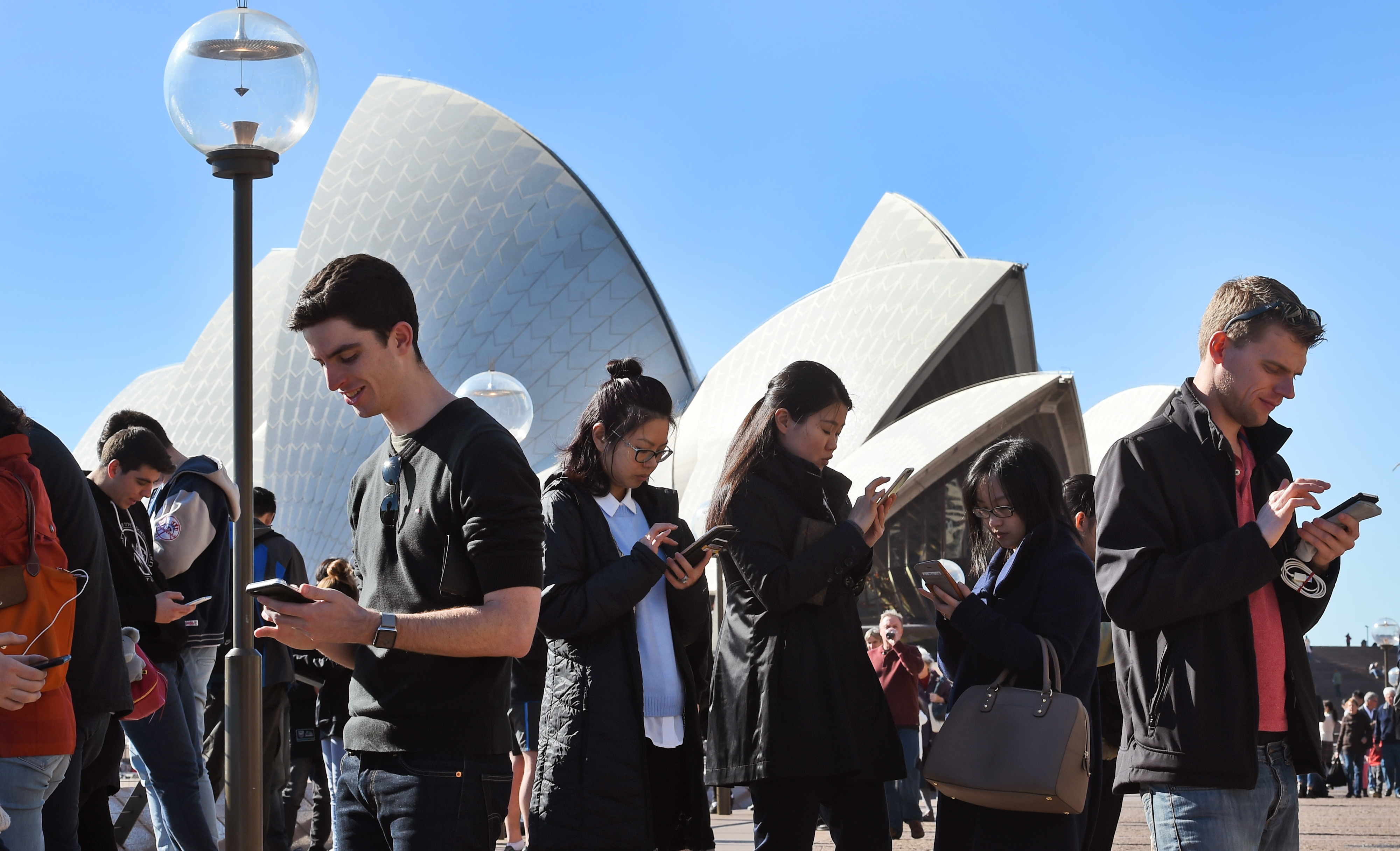 Dozens of people gather to play Pokemon Go in front of the Sydney Opera House on July 15, 2016. The wildly popular mobile app, which is based on a 1990s Nintendo game, has created a global frenzy as players roam the real world looking for cartoon monsters and was launched in Australia last week. / AFP PHOTO / William WEST