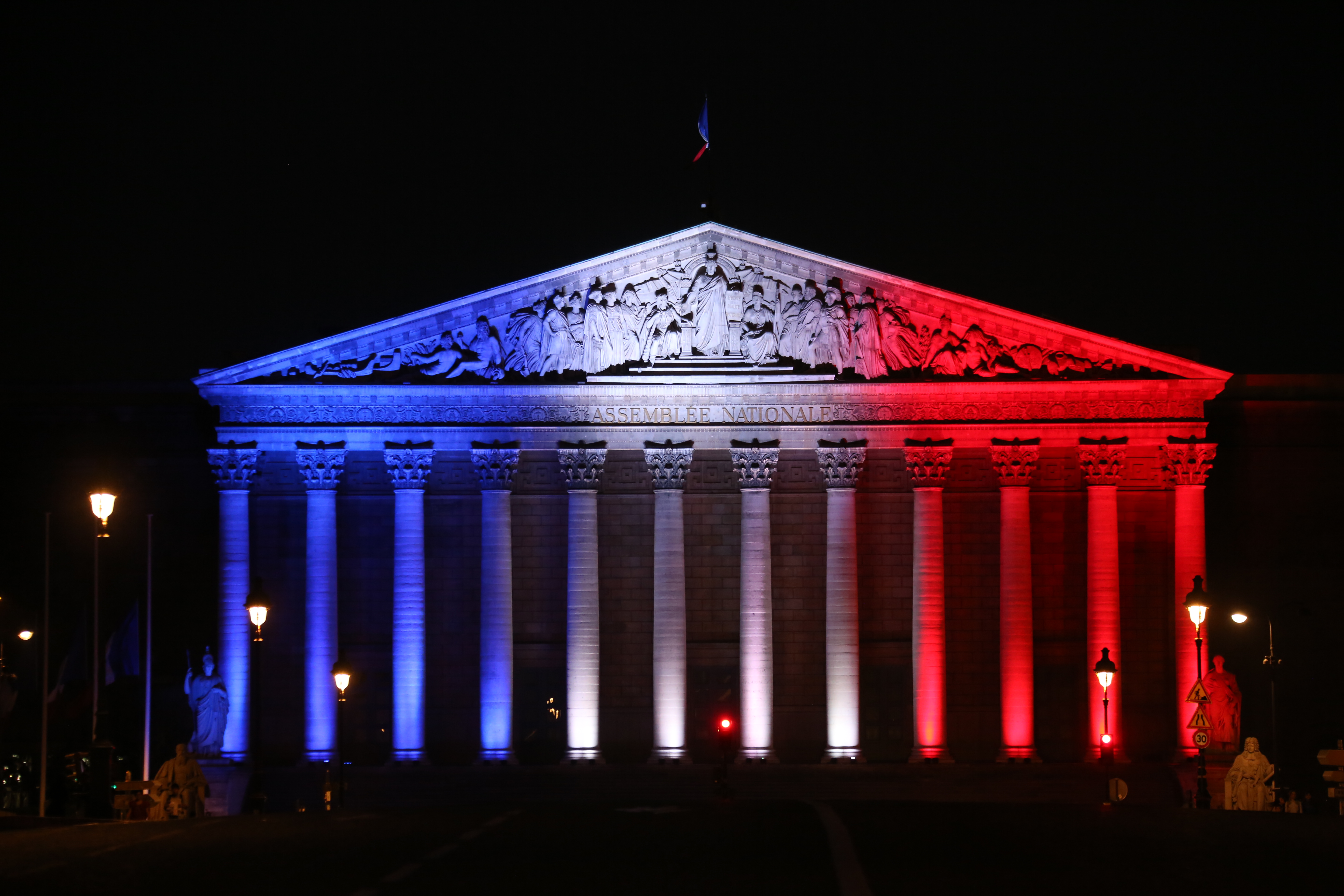 A picture taken on July 26, 2016, shows the National Assembly's palais Bourbon in Paris illuminated in the French flag colours in tribute to the victims of the attack in the Normandy city of Saint-Etienne-du-Rouvray, in which a priest was killed in the city's church, in the latest of a string of attacks against Western targets claimed by or blamed on the Islamic State jihadist group. French President said that two men who attacked a church and slit the throat of a priest had "claimed to be from Daesh", using the Arabic name for the Islamic State group. Police said they killed two hostage-takers in the attack in the Normandy town of Saint-Etienne-du-Rouvray, 125 kilometres (77 miles) north of Paris. / AFP PHOTO / LUDOVIC MARIN