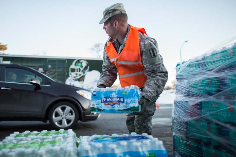 (FILES) This file photo taken on March 4, 2016 shows  Steve Hepler of the Michigan National Guard preparing to load water into a vehicle at a water distribution center in Flint, Michigan. Signaling that their probe is expanding, authorities in the US state of Michigan filed criminal charges on July 29, 2016, against six current and former state officials, over lead water contamination in the city of Flint. "Many things went tragically wrong in Flint. Some failed to act," said Michigan State Attorney General Bill Schuette, "Some intentionally altered figures, and covered up." / AFP PHOTO / Geoff Robins