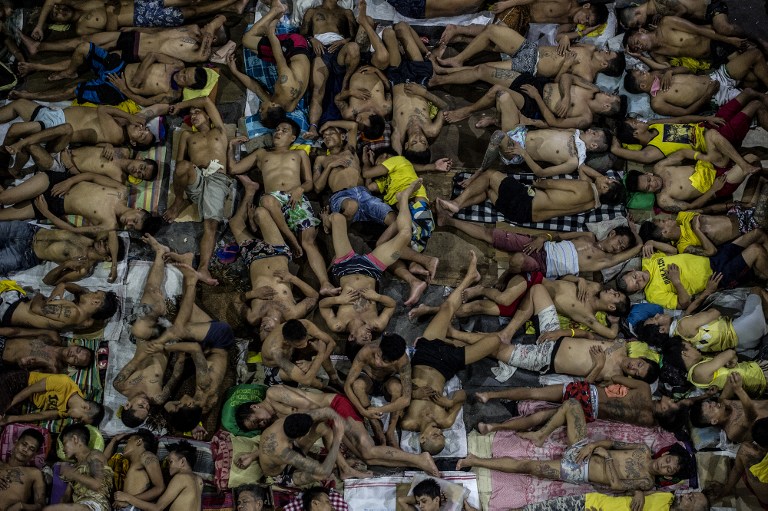 In this photo taken on July 19, 2016 inmates sleep on the ground of an open basketball court inside the Quezon City jail at night in Manila. There are 3,800 inmates at the jail, which was built six decades ago to house 800, and they engage in a relentless contest for space. Men take turns to sleep on the cracked cement floor of an open-air basketball court, the steps of staircases, underneath beds and hammocks made out of old blankets. / AFP PHOTO / NOEL CELIS /