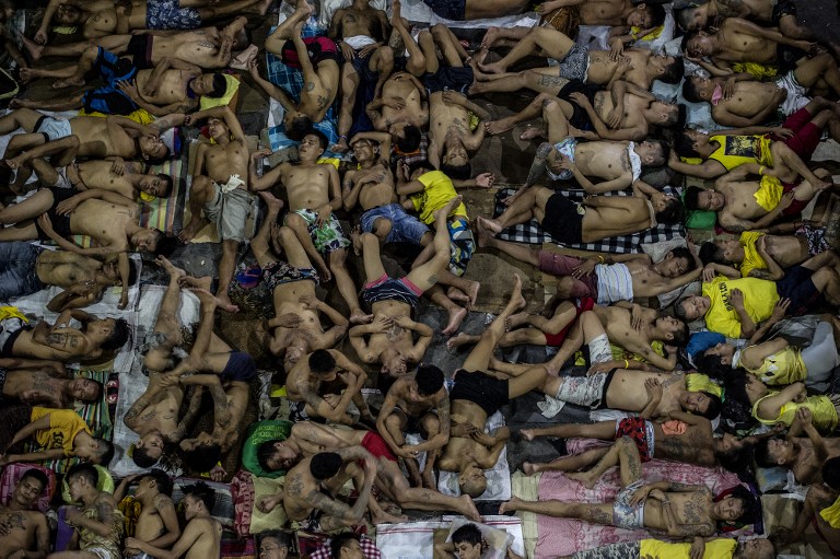 In this photo taken on July 19, 2016 inmates sleep on the ground of an open basketball court inside the Quezon City jail at night in Manila. There are 3,800 inmates at the jail, which was built six decades ago to house 800, and they engage in a relentless contest for space. Men take turns to sleep on the cracked cement floor of an open-air basketball court, the steps of staircases, underneath beds and hammocks made out of old blankets. / AFP PHOTO / NOEL CELIS / 