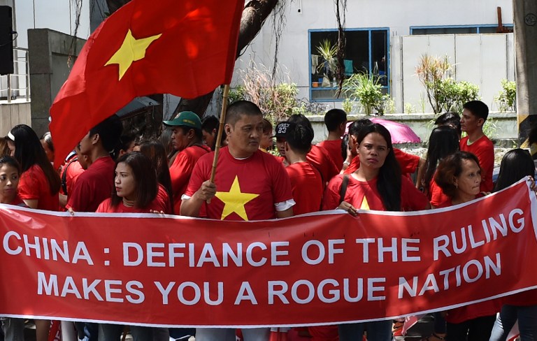 Filipino and Vietnamese protesters displays an anti-China banner next to a Vietnamese national flag (L) during a call on China to respect their rights in the disputed South China Sea, in front of the Chinese consular office in Manila on August 6, 2016. The Philippines told its fishermen on August 3 to steer clear of a fishing ground in the disputed South China Sea to avoid harassment from Chinese authorities. The warning came despite a recent ruling by a UN-backed tribunal in favour of the Philippines, as it dismissed China's territorial claims to large swathes of the waters. Vietnam, Malaysia, Brunei and Taiwan also have claims to the sea, through which over 5 trillion USD in annual trade passes. / AFP PHOTO / TED ALJIBE