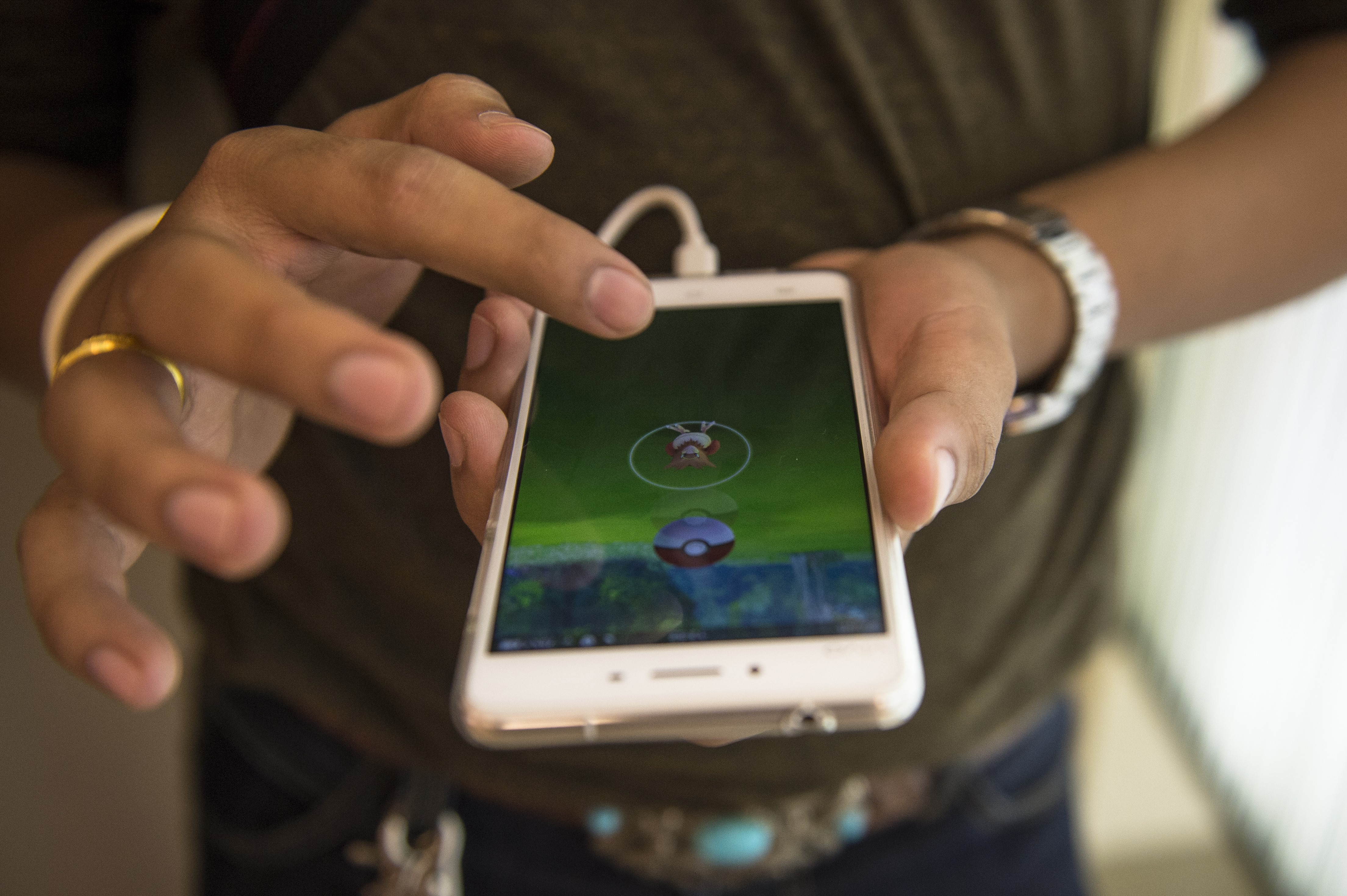 A gamer plays Pokemon Go on his mobile phone in a shopping mall in Bangkok on August 9, 2016. Pokemon Go's debut in Thailand has alarmed the country's generals, prompting the kingdom's junta chief to warn youngsters against playing too much and the army to ban the game from barracks. The mobile app was made available in Thailand on August 6, delighting many in a country where Japanese subcultures have a significant following. / AFP PHOTO / LILLIAN SUWANRUMPHA