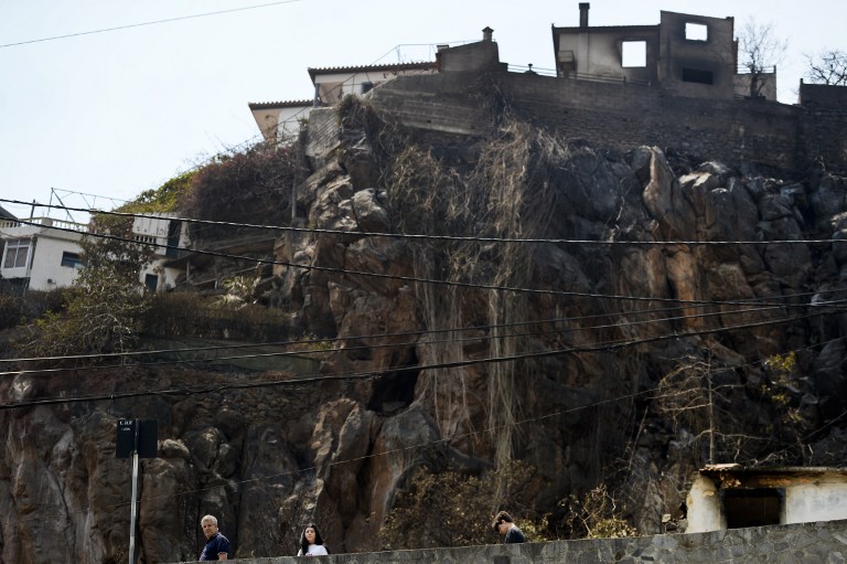 People walk past an area devestated by fire in Funchal, Madeira island on August 11, 2016. The situation on the fire front that claimed the lives of three people on the Portuguese archipelago of Madeira was seemingly under control today but authorities fear a return of the flames with continuing violent winds. / AFP PHOTO / PATRICIA DE MELO MOREIRA
