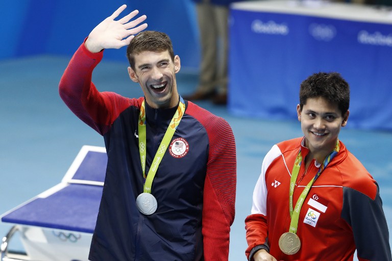 Silver medallist USA's Michael Phelps (L) waves nex to gold medallist Singapore's Schooling Joseph during the medal ceremony of the Men's 100m Butterfly Final during the swimming event at the Rio 2016 Olympic Games at the Olympic Aquatics Stadium in Rio de Janeiro on August 12, 2016. / AFP PHOTO / Odd Andersen