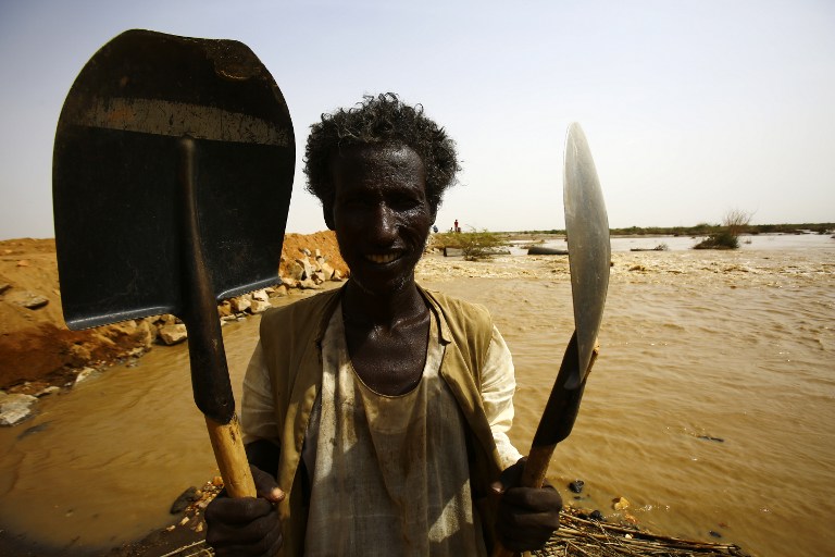 A Sudanese farmer poses with his shovels next to a highway that has been damaged due to heavy flooding on August 15, 2016, in the impoverished eastern state of Kasala bordering Eritrea. Thousands of houses have been destroyed and several villages submerged after flooding triggered by torrential rainfall killed 100 people across Sudan, officials and an AFP photographer said. / AFP PHOTO / ASHRAF SHAZLY