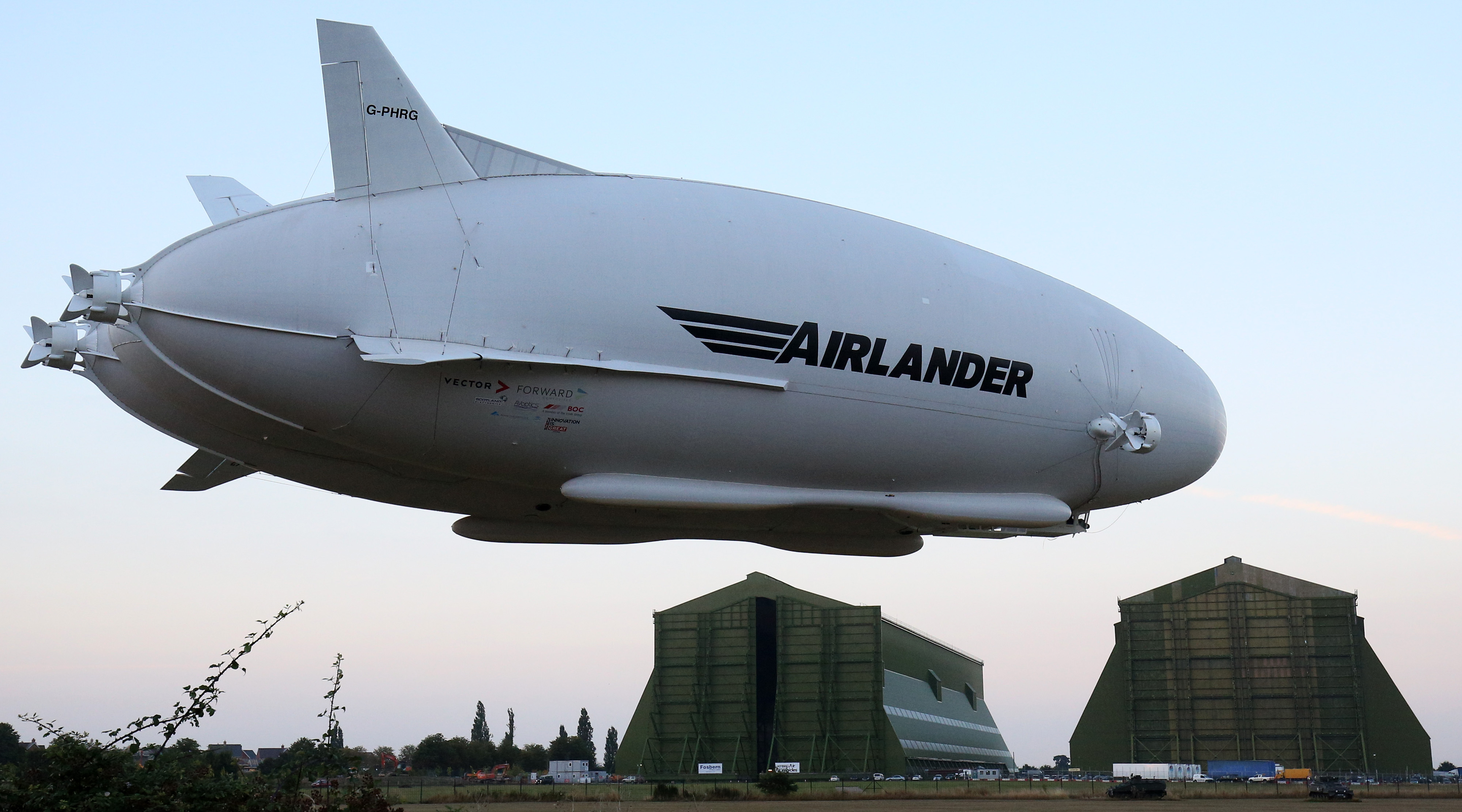 The Hybrid Air Vehicles HAV 304 Airlander 10 hybrid airship is seen with hangars in the background on its maiden flight at Cardington Airfield near Bedford, north of London, on August 17, 2016. The Hybrid Air Vehicles 92-metre long, 43.5-metre wide Airlander 10, billed as the world's longest aircraft, lifted off for the first time from an airfield north of London. The Airlander 10 has a large helium-filled fabric hull and is propelled by four turbocharged diesel engines. According to the company it can stay airborne for up to five days at a time if manned, and for over 2 weeks unmanned with a cruising speed of just under 150 km per hour and a payload capacity of up to 10,000 kg. / AFP PHOTO / JUSTIN TALLIS