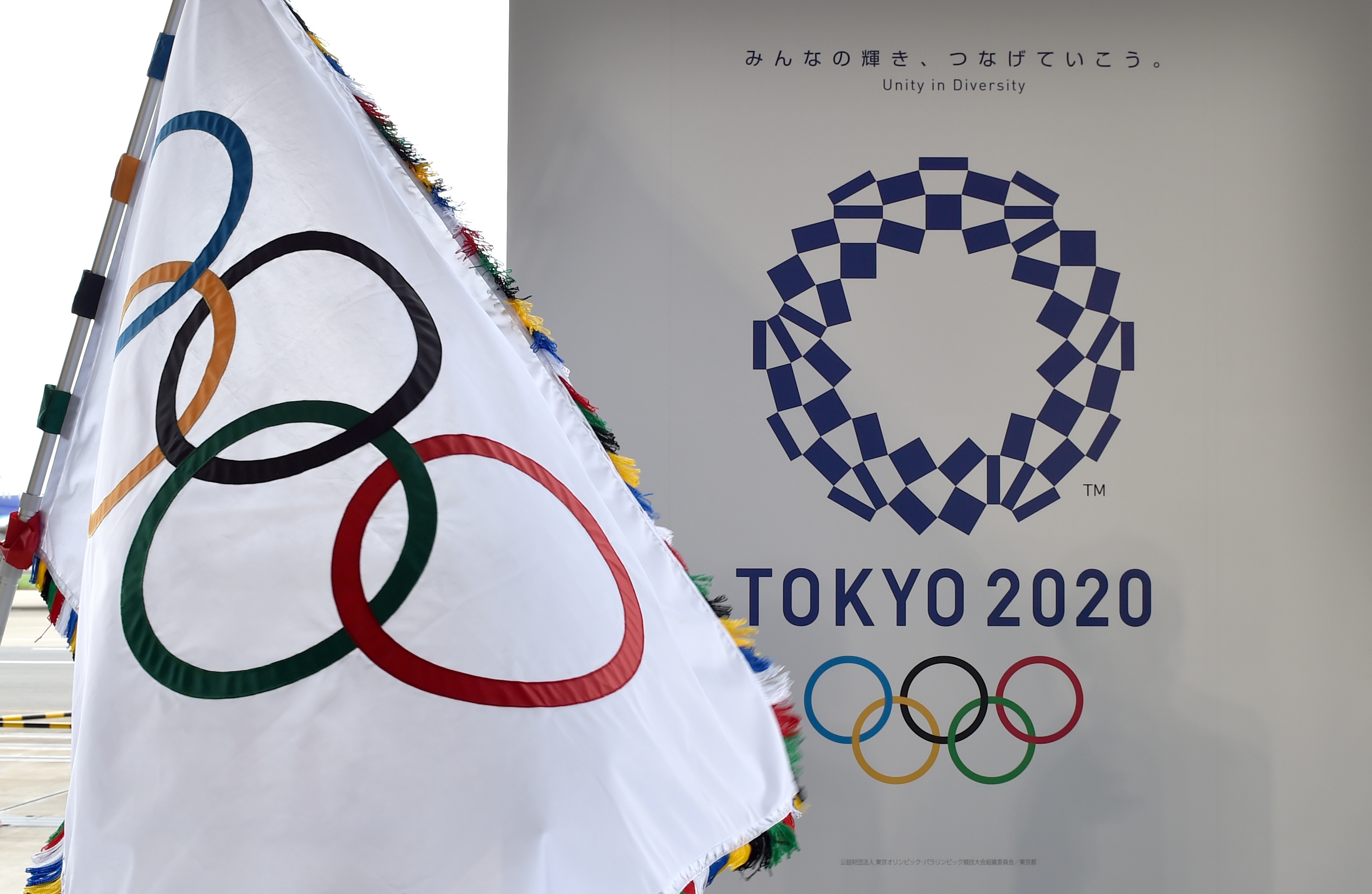The Olympic flag (L) and the logo of the Tokyo 2020 are displayed during the official flag arrival ceremony at the Tokyo's Haneda airport on August 24, 2016. The Olympic flag arrived in Tokyo on August 24, as Japan's capital gears up to host the 2020 Games, with officials promising smooth sailing after Rio's sometimes shaky 2016 instalment. / AFP PHOTO / KAZUHIRO NOGI