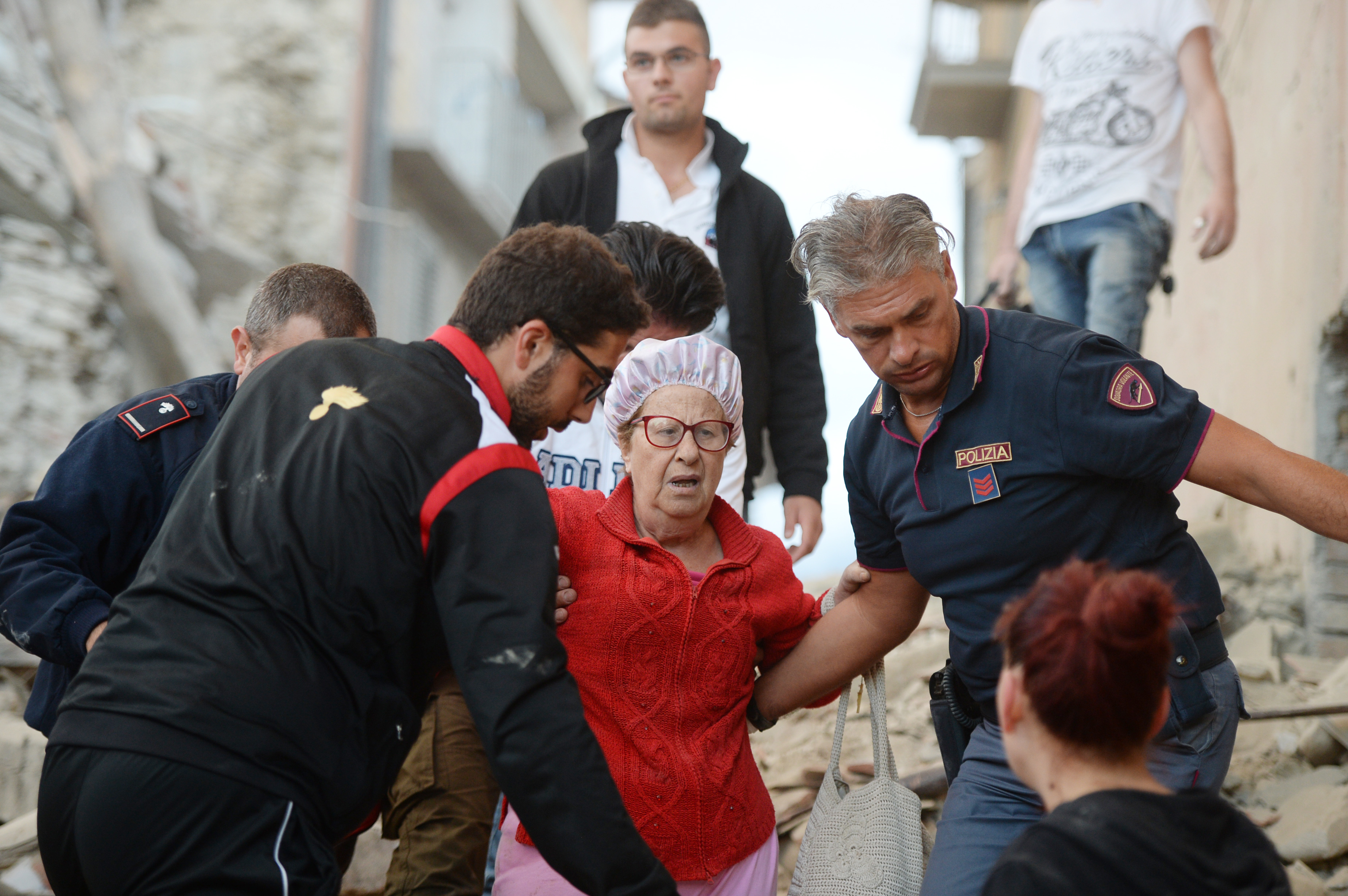 Rescuers help a woman among damaged buildings after a strong heartquake hit Amatrice on August 24, 2016. Central Italy was struck by a powerful, 6.2-magnitude earthquake in the early hours, which has killed at least three people and devastated dozens of mountain villages. Numerous buildings had collapsed in communities close to the epicenter of the quake near the town of Norcia in the region of Umbria, witnesses told Italian media, with an increase in the death toll highly likely. / AFP PHOTO / FILIPPO MONTEFORTE