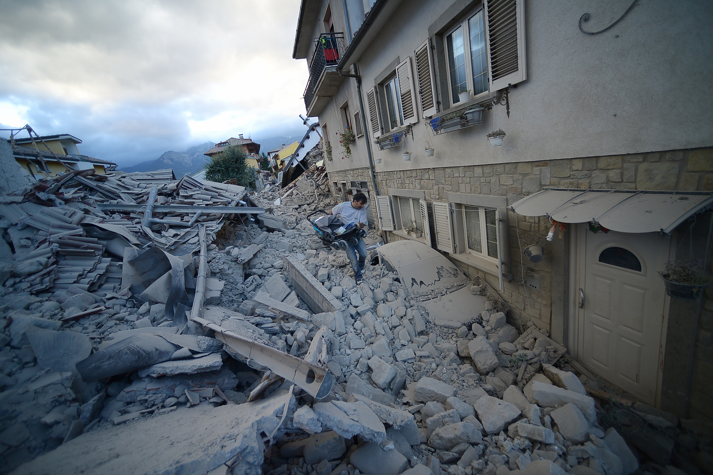 A resident carries a pram among damaged buildings after a strong heartquake hit Amatrice on August 24, 2016. Central Italy was struck by a powerful, 6.2-magnitude earthquake in the early hours, which has killed at least three people and devastated dozens of mountain villages. Numerous buildings had collapsed in communities close to the epicenter of the quake near the town of Norcia in the region of Umbria, witnesses told Italian media, with an increase in the death toll highly likely. / AFP PHOTO / FILIPPO MONTEFORTE