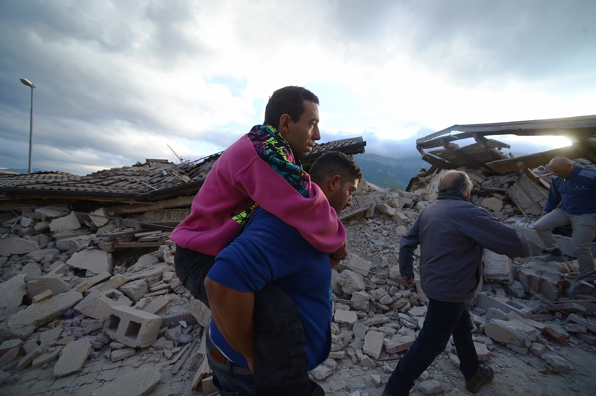 residents help each other among damaged buildings after a strong heartquake hit Amatrice on August 24, 2016. Central Italy was struck by a powerful, 6.2-magnitude earthquake in the early hours, which has killed at least three people and devastated dozens of mountain villages. Numerous buildings had collapsed in communities close to the epicenter of the quake near the town of Norcia in the region of Umbria, witnesses told Italian media, with an increase in the death toll highly likely. / AFP PHOTO / FILIPPO MONTEFORTE