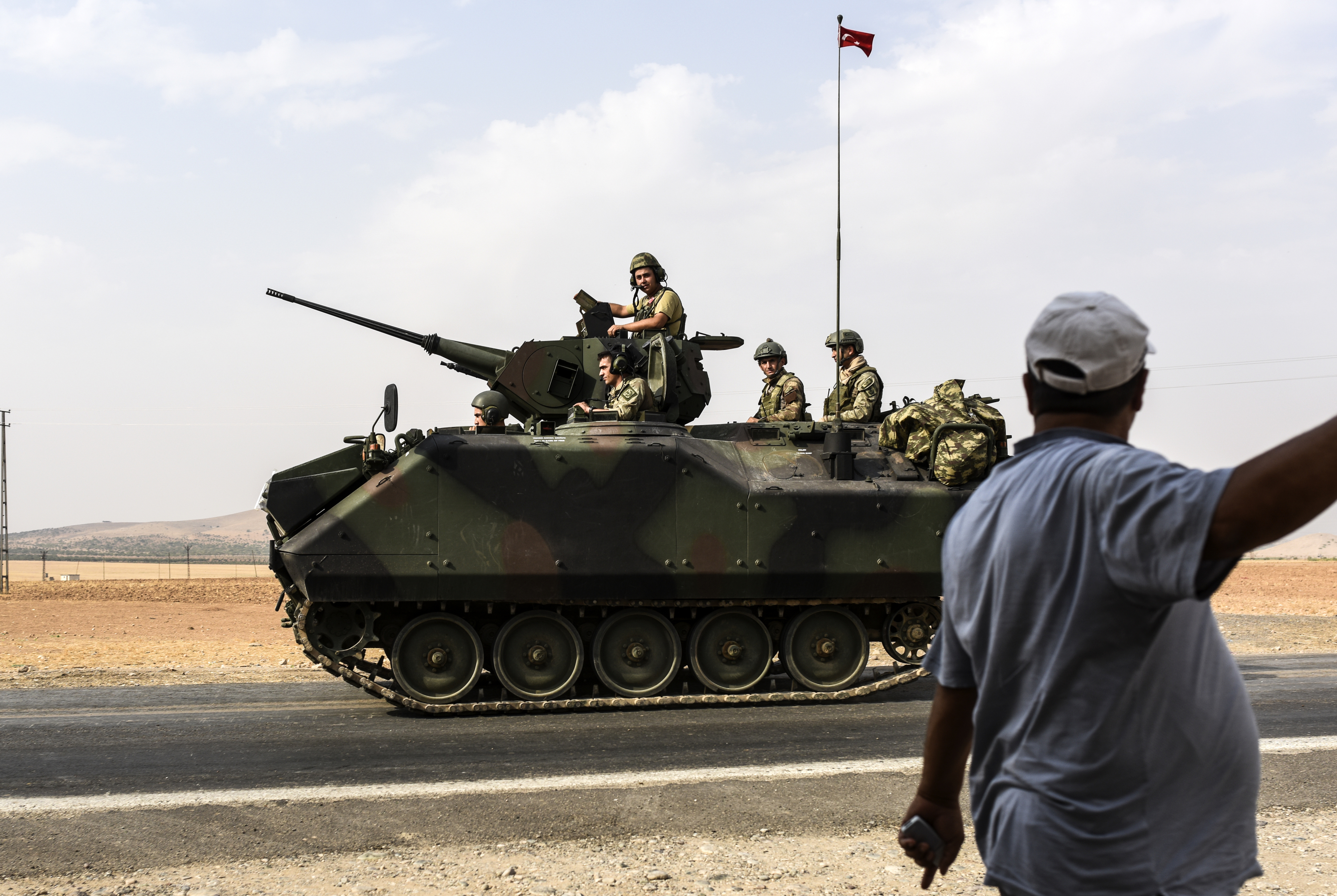 A Turkish man stands as a Turkish tank convoy drives to Syria from the Turkish Syrian border city of Karkamis in the southern region of Gaziantep, on August 26, 2016.  Turkey shelled Kurdish militia fighters in Syria on August 26 on the second day of a major military operation inside the country, saying they were failing to observe a deal with the US to stop advancing in jihadist-held territory. Turkey's army backed by international coalition air strikes launched an operation involving fighter jets and elite ground troops to drive Islamic State jihadists out of the border area. / AFP PHOTO / BULENT KILIC