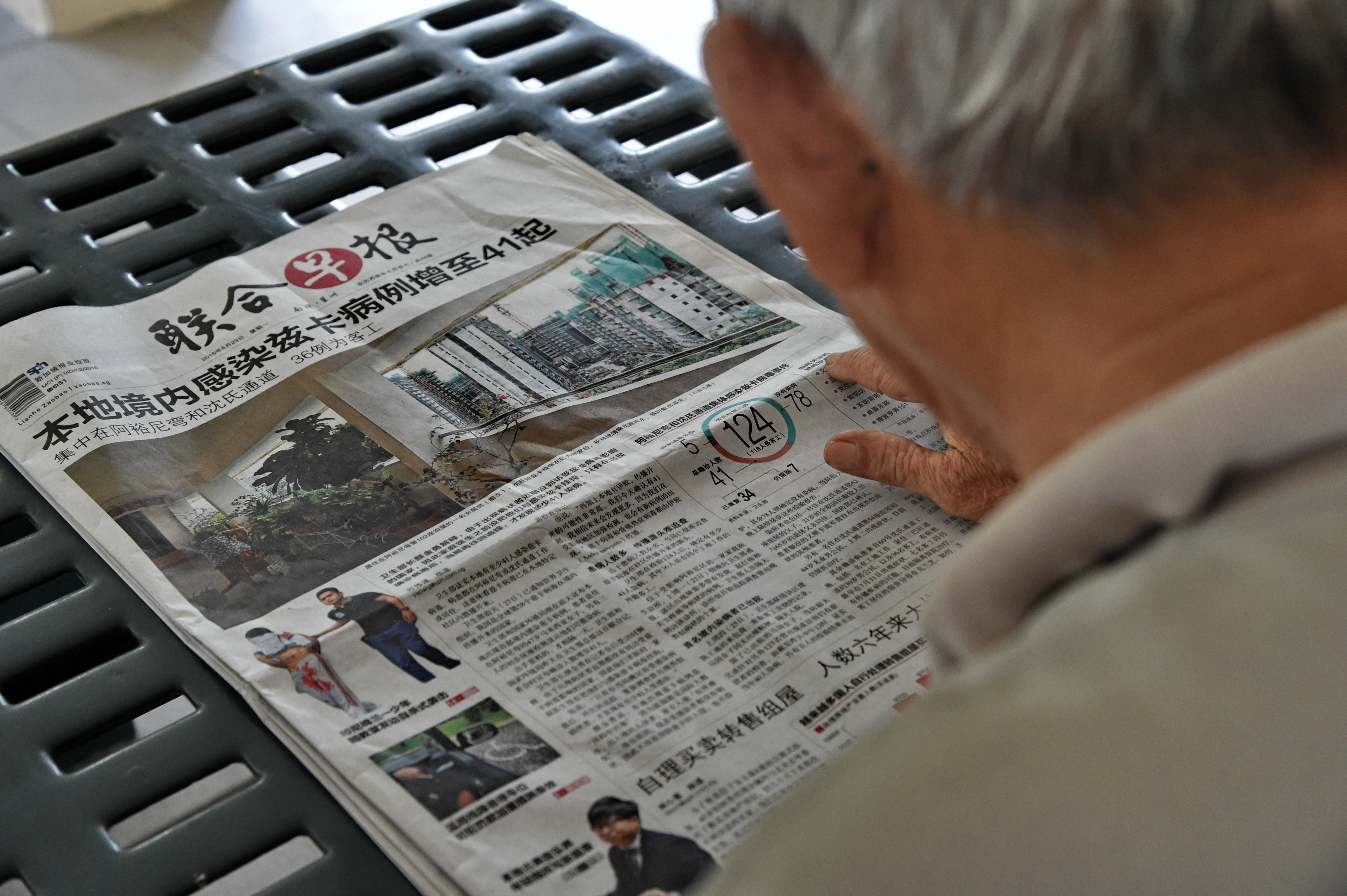A resident reads a local newspaper reporting on locally transmitted cases of the Zika virus, in a residential block at the Aljunied Crescent neighbourhood in Singapore on August 29, 2016. Singapore on August 28 confirmed 41 locally transmitted cases of the Zika virus, which can cause deformities in unborn babies, and said more infections are likely. / AFP PHOTO / ROSLAN RAHMAN