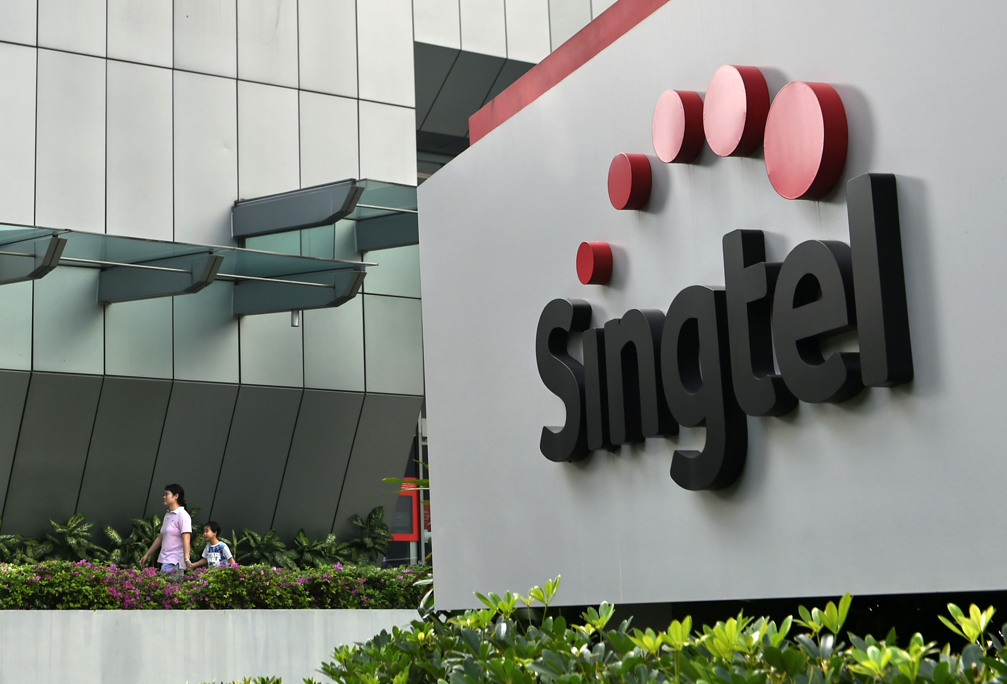 A woman and a child walk out of the Singapore Telecommunications (Singtel) building in Singapore on February 12, 2016. Singtel reported a 1.7 per cent fall in third-quarter net profit of 683 million US dollar for the three months ended December, compared with 694 million US dollar a year ago, as adverse currency movements and investments offset growing mobile data usage by its customers. AFP PHOTO / ROSLAN RAHMAN / AFP PHOTO / ROSLAN RAHMAN