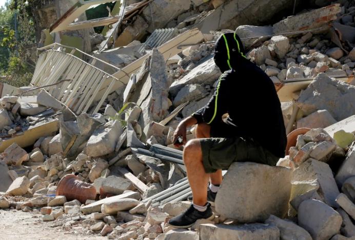 A man sits on the rubble of a collapsed building following an earthquake in Amatrice, central Italy, August 26, 2016. REUTERS/Ciro De Luca