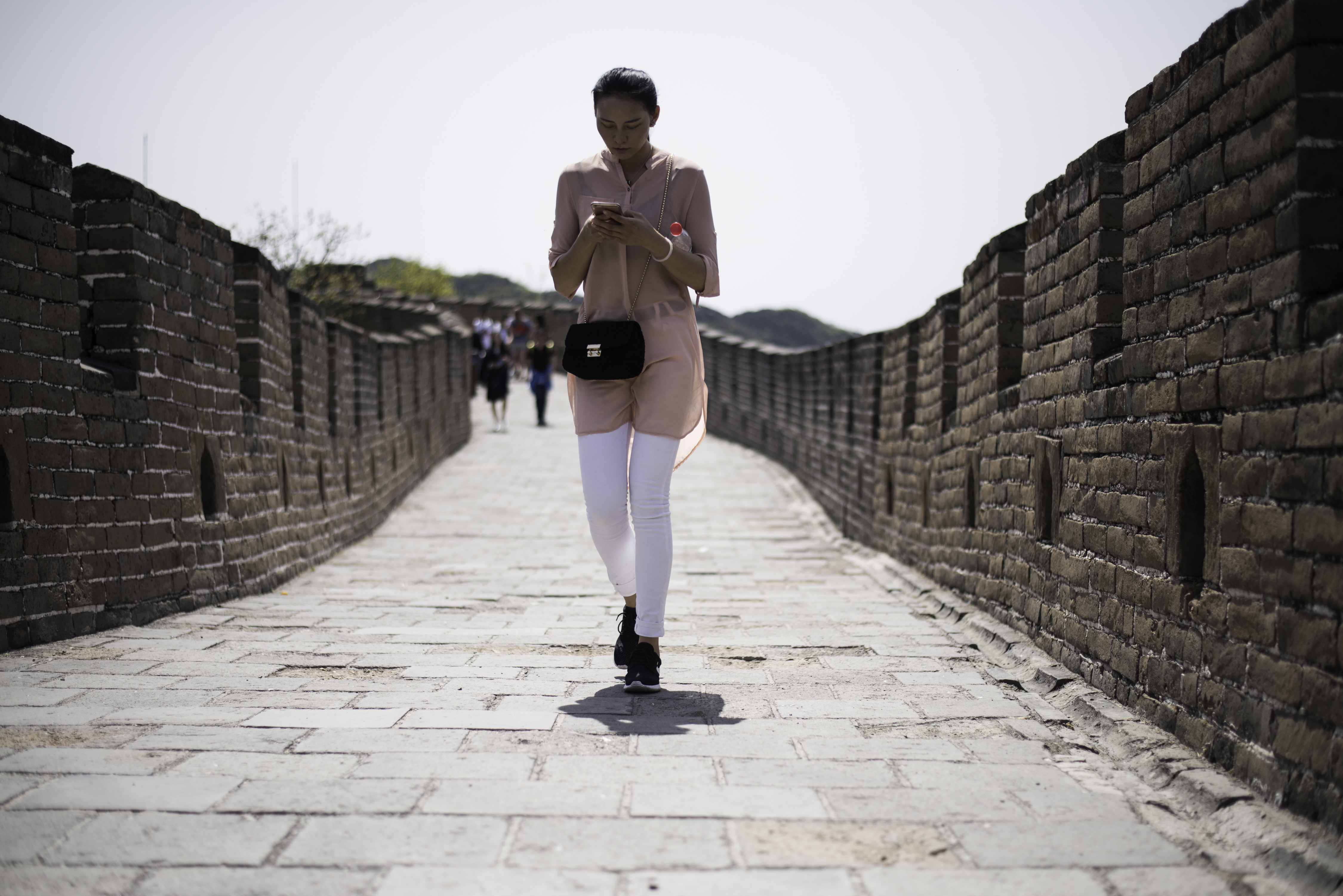 A Chinese lady walks as she types on her smartphone on the Great Wall in Mutianyu, near in Beijing on April 23, 2016. / AFP PHOTO / FRED DUFOUR