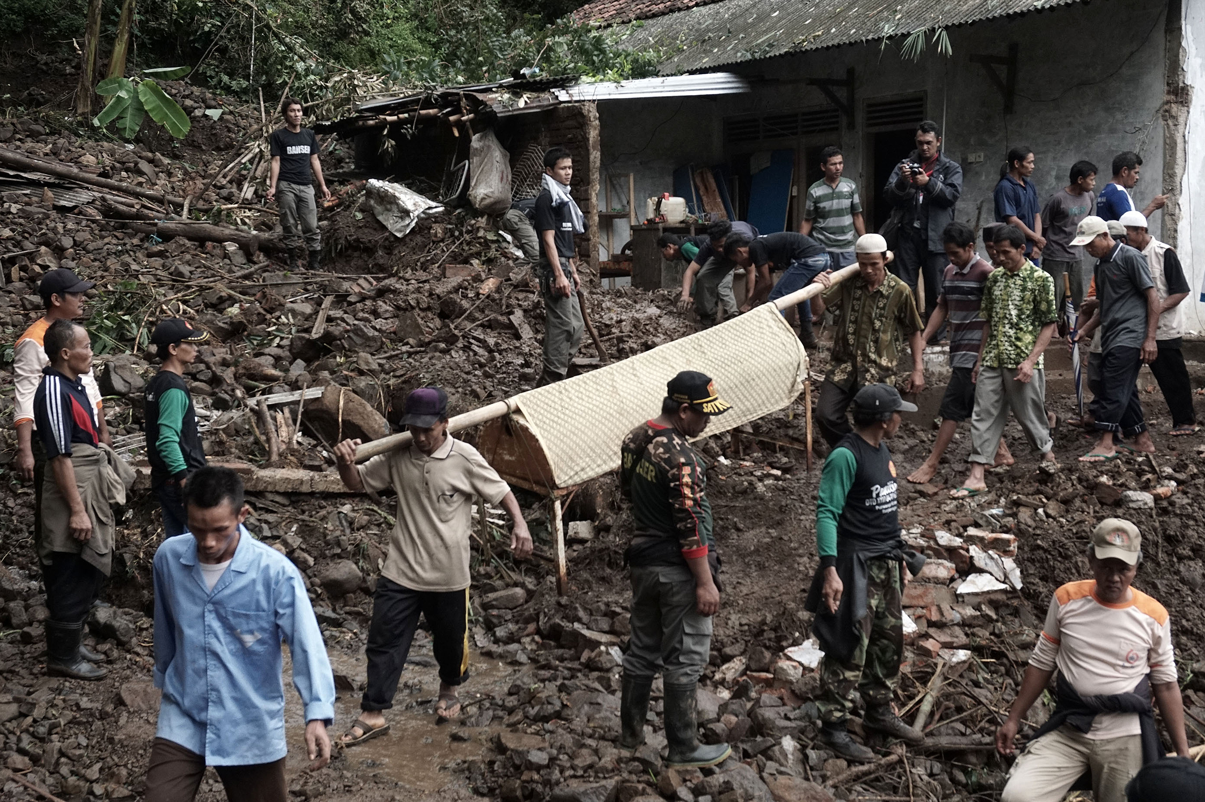 Indonesian villagers and search and rescue team members carry out the body of a landslide victim at Gumelem Kulon village in Banjarnegara on June 19, 2016. Flash flooding and landslides in Indonesia have killed 24 and left more than two dozen missing, an official said on June 19, with mud avalanches burying people inside their homes. / AFP PHOTO / ROHMAT SYARIF