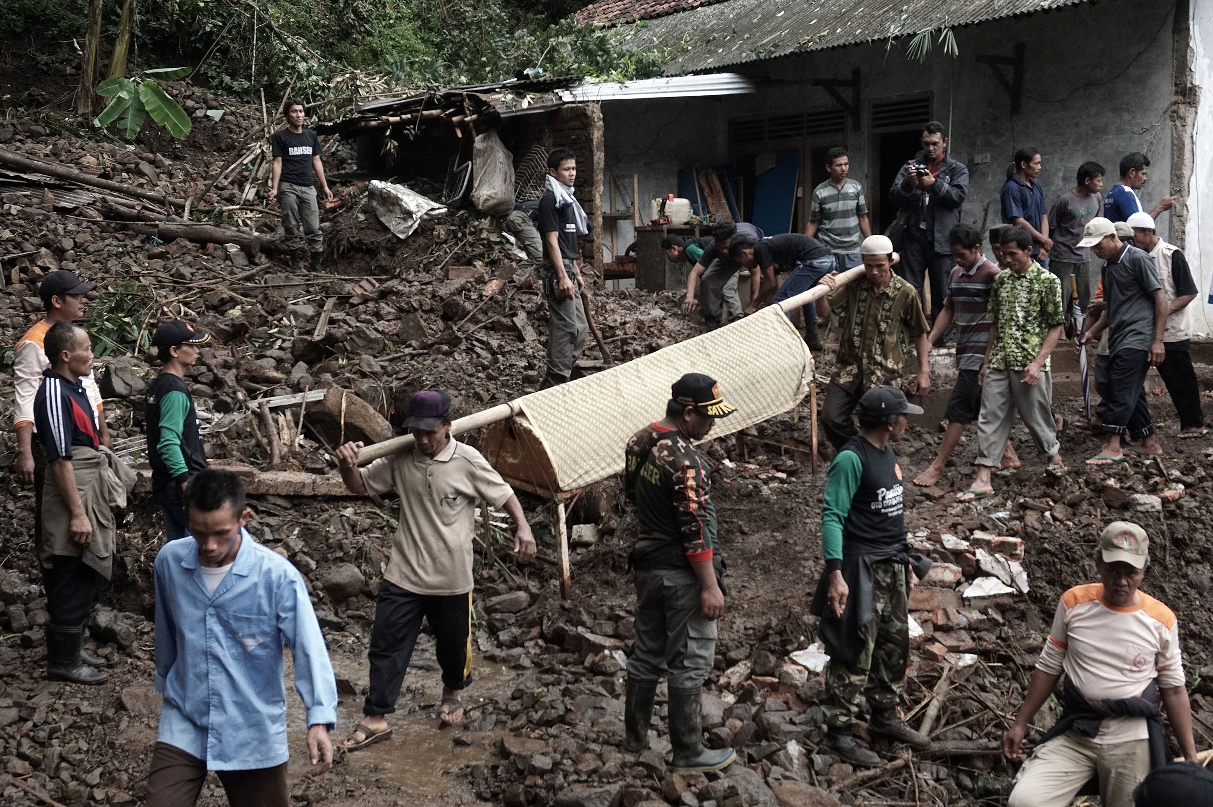 Indonesian villagers and search and rescue team members carry out the body of a landslide victim at Gumelem Kulon village in Banjarnegara on June 19, 2016.   Flash flooding and landslides in Indonesia have killed 24 and left more than two dozen missing, an official said on June 19, with mud avalanches burying people inside their homes. / AFP PHOTO / ROHMAT SYARIF