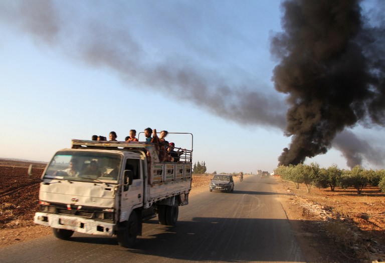 Syrians fleeing from the town of Souran, in northern Hama, drive past burning vehicles on September 1, 2016, after fighters from the Jund al-Aqsa Islamist Brigade took control of the town from Syrian government forces. A coalition of rebels and jihadists quickly advanced this week in the province of Hama, in central Syria, which is largely controlled by the regime forces, and has captured a number of towns, according to the Britain-based Syrian Observatory for Human Rights. On August 29 allied insurgent jihadist groups, including the influential Jund al-Aqsa, launched an offensive with the aim of taking Hama airport, where military helicopters take off to knock the enemies of the regime on other fronts. / AFP PHOTO / Omar haj kadour