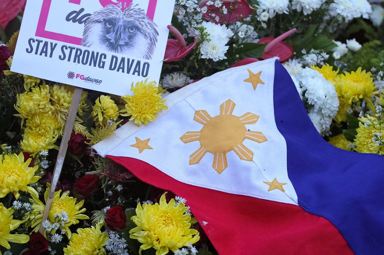 A national flag is placed among flowers as residents offer prayers for bomb blast victims at a night market, during a memorial at the site in Davao City, on the southern island of Mindanao on September 3, 2016.  Philippine authorities blamed a notorious group of Islamic militants for the bombing of a night market in President Rodrigo Duterte's home town that killed at least 14 people. / AFP PHOTO / STR
