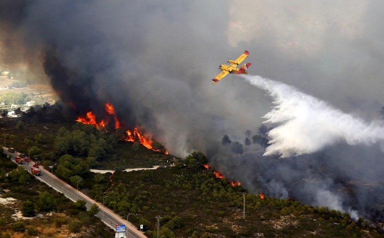 A seaplane drops water over a wildfire next to a residential area along the coastline near the Spanish resort of Javea, Valencia region, on September 5, 2016. More than 1,000 people were evacuated after a wildfire fuelled by intense heat roared through brush surrounding a popular tourist resort on Spain's Costa Blanca, officials said today.  / AFP PHOTO / Manuel Lorenzo