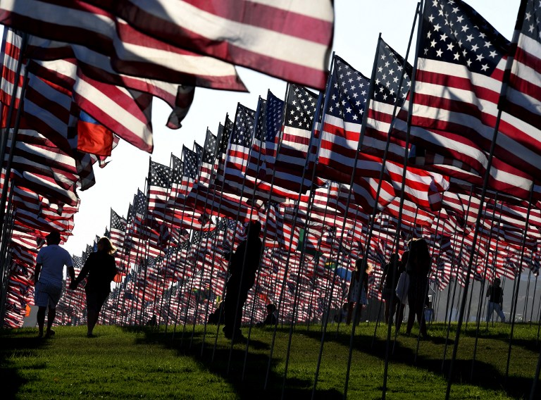 People walk amongst US national flags erected by students and staff from Pepperdine University as they pay their respects to honor the victims of the September 11, 2001 attacks in New York, at their campus in Malibu, California on September 10, 2016.  The students placed aound 3,000 flags in the ground in tribute to the nearly 3,000 victims lost in the attacks almost 15 years ago.  / AFP PHOTO / Mark RALSTON