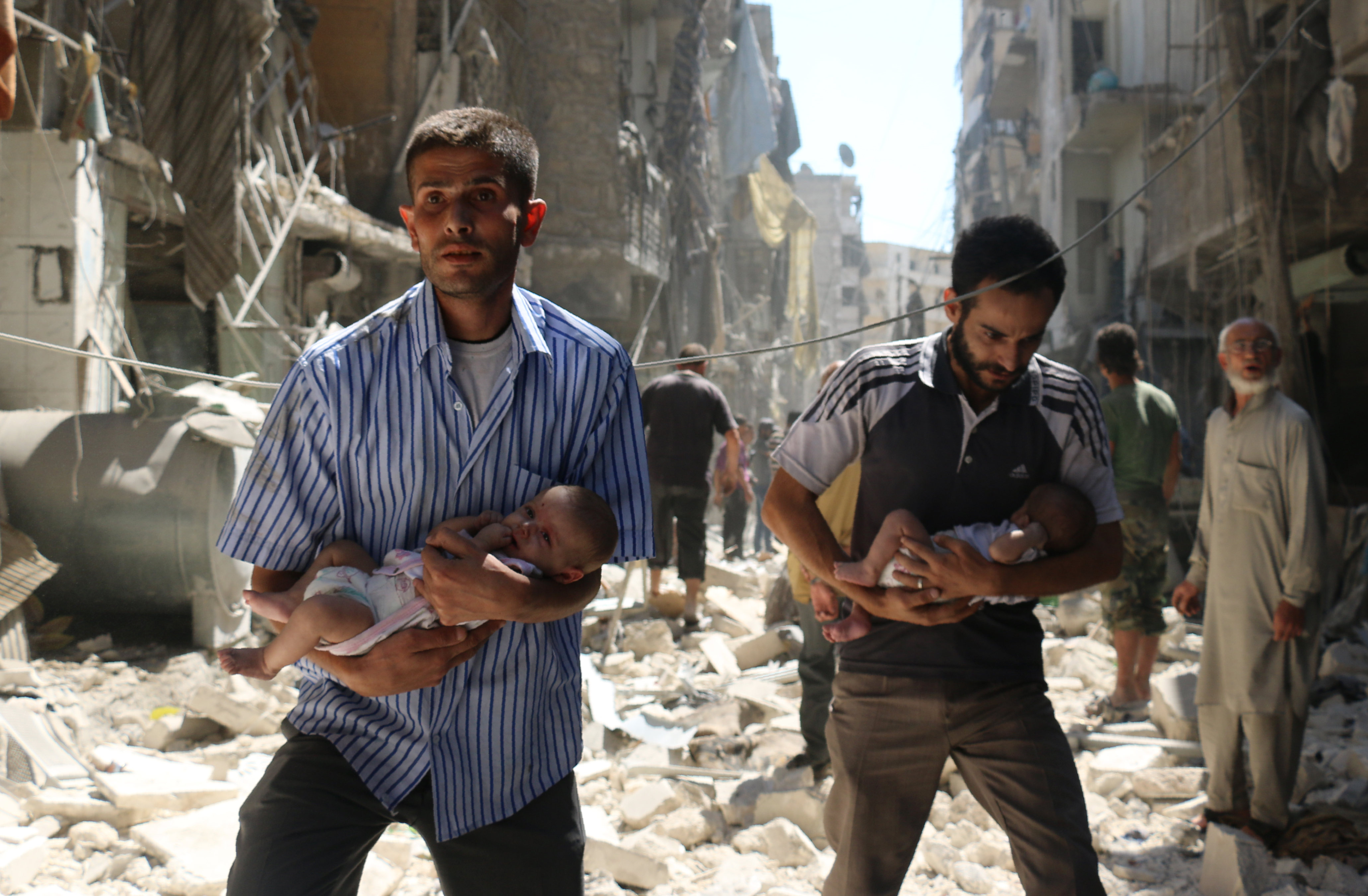 Syrian men carrying babies make their way through the rubble of destroyed buildings following a reported air strike on the rebel-held Salihin neighbourhood of the northern city of Aleppo, on September 11, 2016. Air strikes have killed dozens in rebel-held parts of Syria as the opposition considers whether to join a US-Russia truce deal due to take effect on September 12. / AFP PHOTO / AMEER ALHALBI