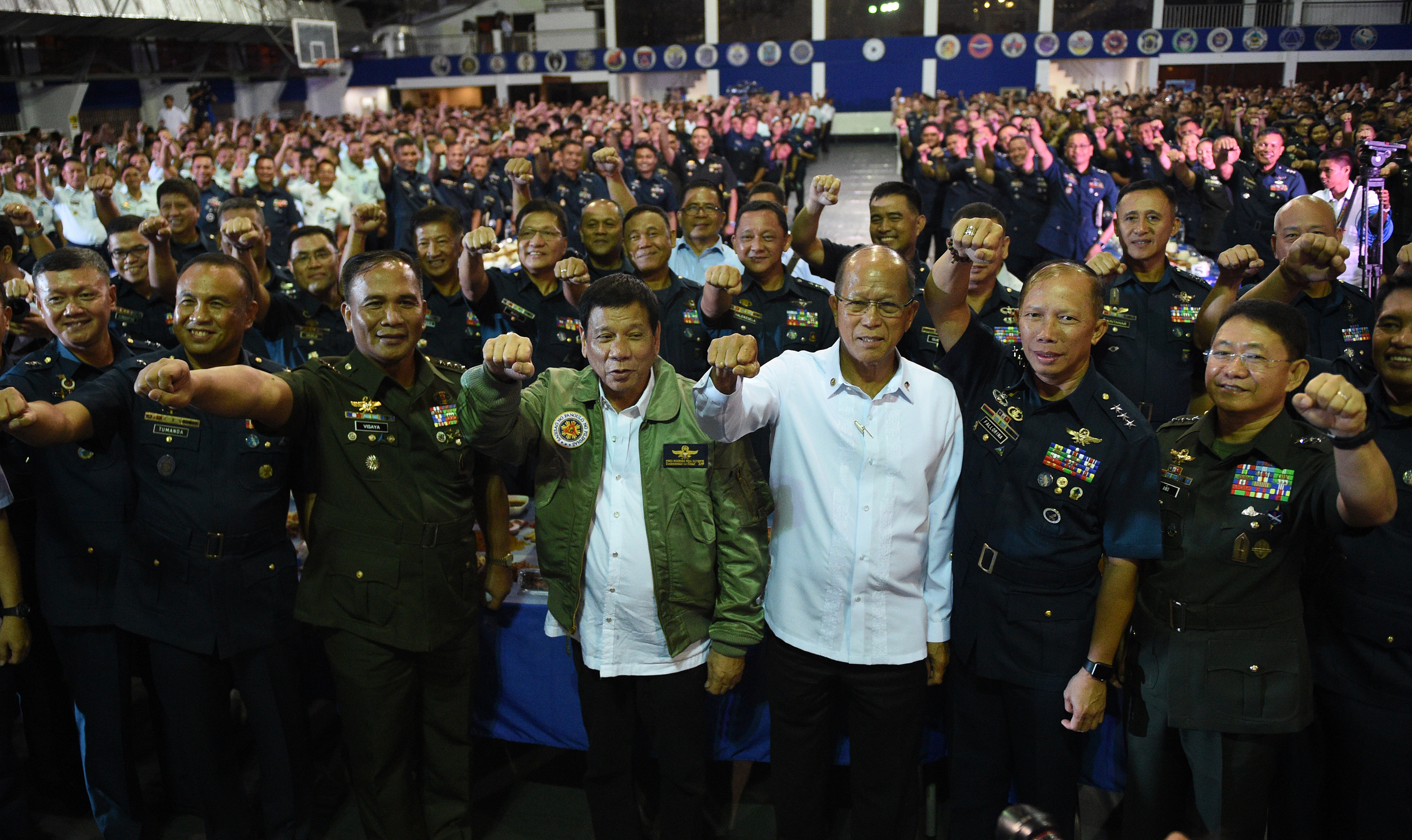 Philippine President Rodrigo Duterte (C) wearing an air force jacket given to him as a gift, poses for photos with Defense Secretary Delfin Lorenzana (4th R) and Military chief General Ricardo Visaya (3rd L) and air force personnel prior to the traditional meal dubbed "boodle fight" during the 250th Presidential Airlift Wing Command anniversary celebrations at Villamor air base in Manila on September 13, 2016. The Philippines assured the United States September 13 it will honour its obligations as a military ally following volleys of profane tirades by unpredictable President Rodrigo Duterte. / AFP PHOTO / TED ALJIBE