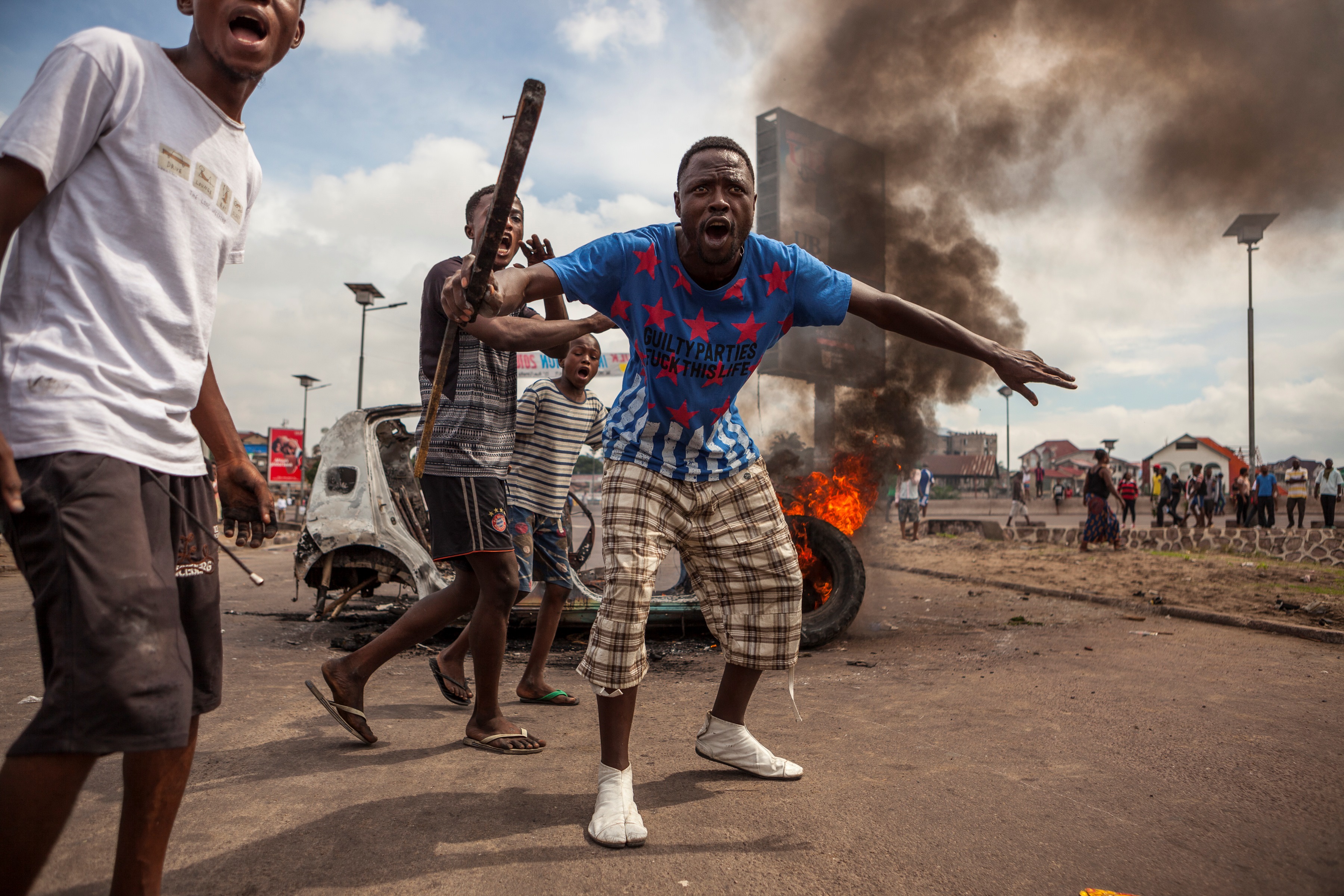 Demonstrators gather in front of a burning car during an opposition rally in Kinshasa on September 19, 2016. Police fired tear gas at scores of opposition supporters rallying in Kinshasa to demand that DR Congo's long-serving President Joseph Kabila step down this year, AFP journalists said. Kabila, who has ruled DR Congo since 2001, is banned under the constitution from running again -- but he has given no sign of intending to give up his job in December. / AFP PHOTO / EDUARDO SOTERAS