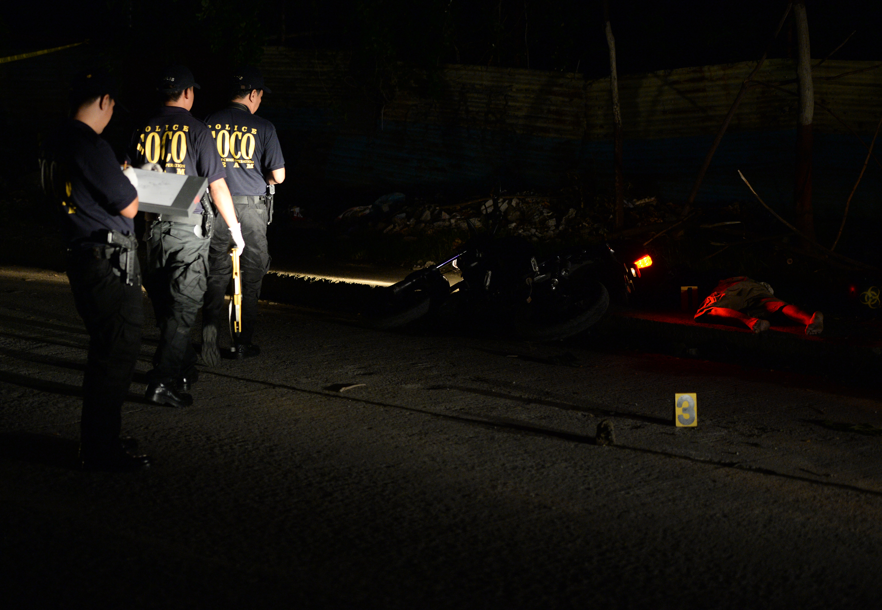 Police members of a Scene of the Crime Operatives (SOCO) team arrive to investigate the site where the bodies of suspected drug pushers (R) lie sprawled on the pavement next to a motorcycle, killed after an encounter with police in the Pasig City district of suburban Manila on September 23, 2016. Philippine President Rodrigo Duterte on September 22 invited the United Nations' chief and international human rights experts to investigate allegations of widespread extrajudicial killings, but insisted they also face him in a public debate. / AFP PHOTO / TED ALJIBE