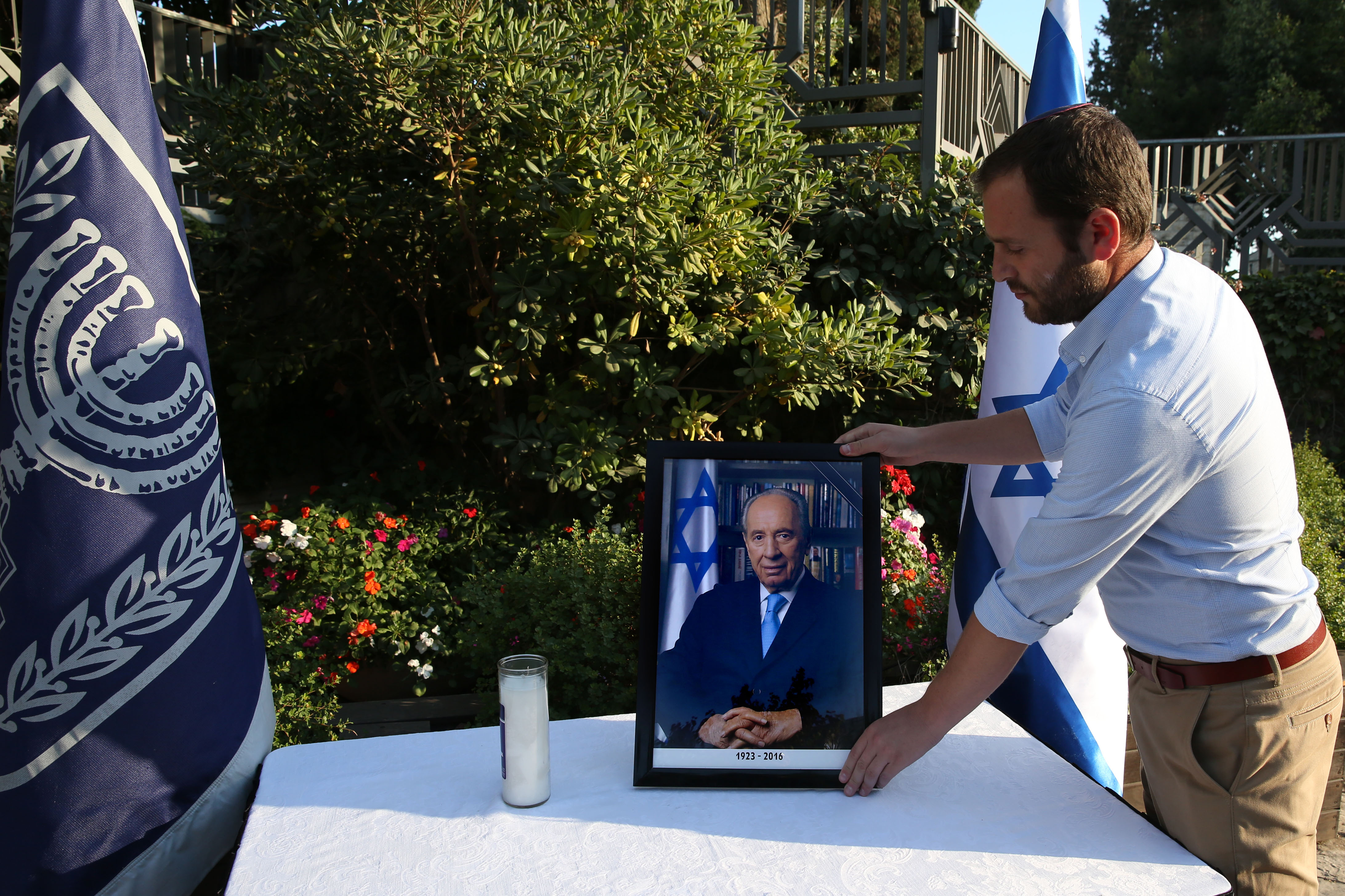 A worker of the Israeli President office places a picture of former Israeli president and Nobel Peace Prize winner Shimon Peres displayed after his death outside the presidential compound in Jerusalem, on September 28, 2016. Israel and global leaders mourned the death of ex-president and Nobel Peace Prize winner Shimon Peres on September 28, 2016 as the country prepared for a funeral expected to be attended by major world figures. Peres, who was 93, held nearly every major office in the country, serving twice as prime minister and also as president, a mostly ceremonial role, from 2007 to 2014.  / AFP PHOTO / GALI TIBBON