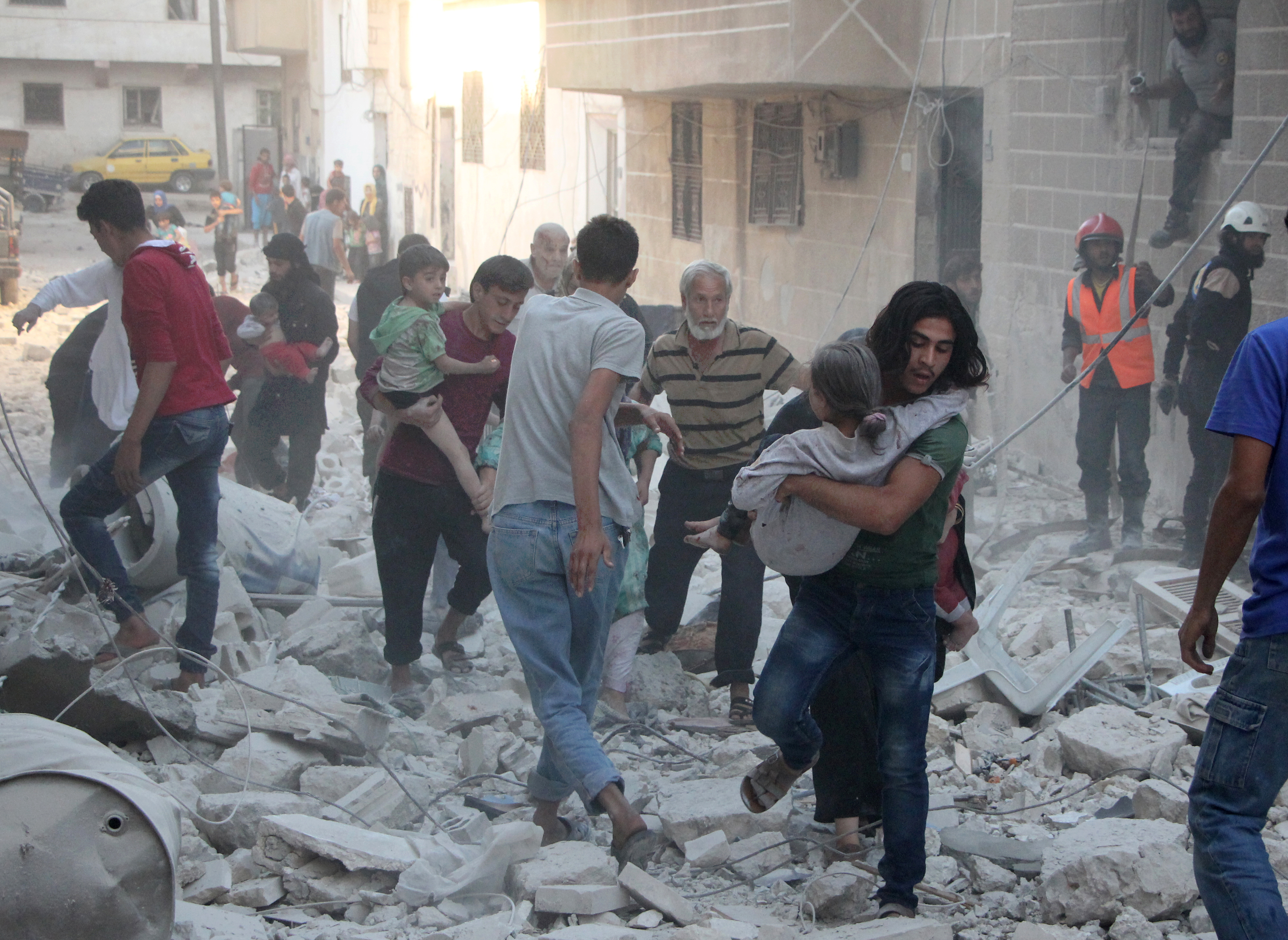 Syrian men carry injured people amid the rubble of destroyed buildings following a reported air strike on the rebel-held northwestern city of Idlib on September 29, 2016. In a statement the Syrian Observatory for Human Rights said that at least five air strikes hit various areas in the city of Idlib. / AFP PHOTO / Omar haj kadour