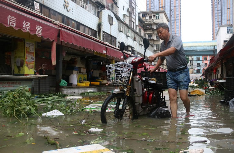 A man pushes a motorbike through a flooded street in Xiamen, in China's eastern Fujian province after Typhoon Meranti made landfall on September 15, 2016. Typhoon Meranti made landfall in Fujian early on September 15, with winds up to 230kph, knocking out electricity in some areas and causing rail delays. / AFP PHOTO / STR /
