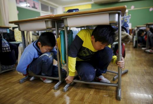 School children take shelter under desks during an earthquake simulation exercise in an annual evacuation drill at an elementary school in Tokyo March 11, 2016, to mark the five-year anniversary of the March 11, 2011 earthquake and tsunami that killed thousands and set off a nuclear crisis. REUTERS/Issei Kato