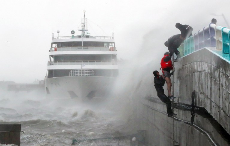 South Korean coast guards try to rescue crew members of a stranded passenger ship in the aftermath of typhoon Chaba in the southern city of Yeosu on October 5, 2016. The typhoon hit the South Korean resort island of Jeju early on October 5, bringing heavy rains that flooded streets, forced flight cancellations and disrupted power to thousands of homes. More than 25,000 houses on the island of Jeju had their power supply disrupted, the Yonhap news agency reported, while Busan city announced the closure of 900 schools. / AFP PHOTO / YONHAP / YONHAP 