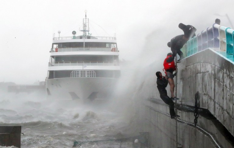 South Korean coast guards try to rescue crew members of a stranded passenger ship in the aftermath of typhoon Chaba in the southern city of Yeosu on October 5, 2016. The typhoon hit the South Korean resort island of Jeju early on October 5, bringing heavy rains that flooded streets, forced flight cancellations and disrupted power to thousands of homes. More than 25,000 houses on the island of Jeju had their power supply disrupted, the Yonhap news agency reported, while Busan city announced the closure of 900 schools. / AFP PHOTO / YONHAP / YONHAP