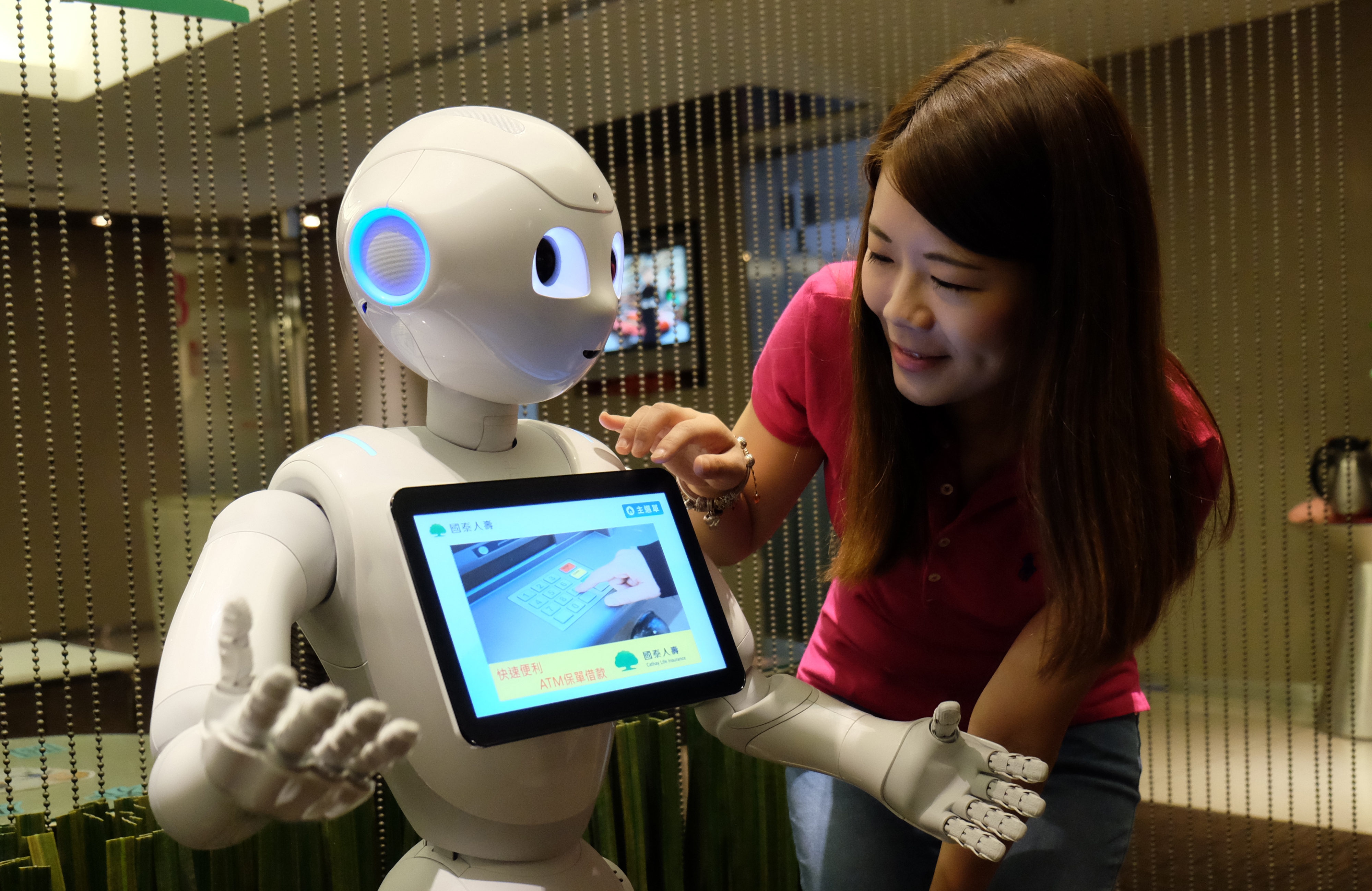 A woman gives a comand to a robot named Pepper during a press conference organized by Cathay Financial Holdings in Taipei on October 6, 2016.  A mini robot called "Pepper" started work alongside human colleagues at banks and an insurance company in Taiwan, enlisted with entertaining bored customers -- and giving them the hard sell. / AFP PHOTO / SAM YEH