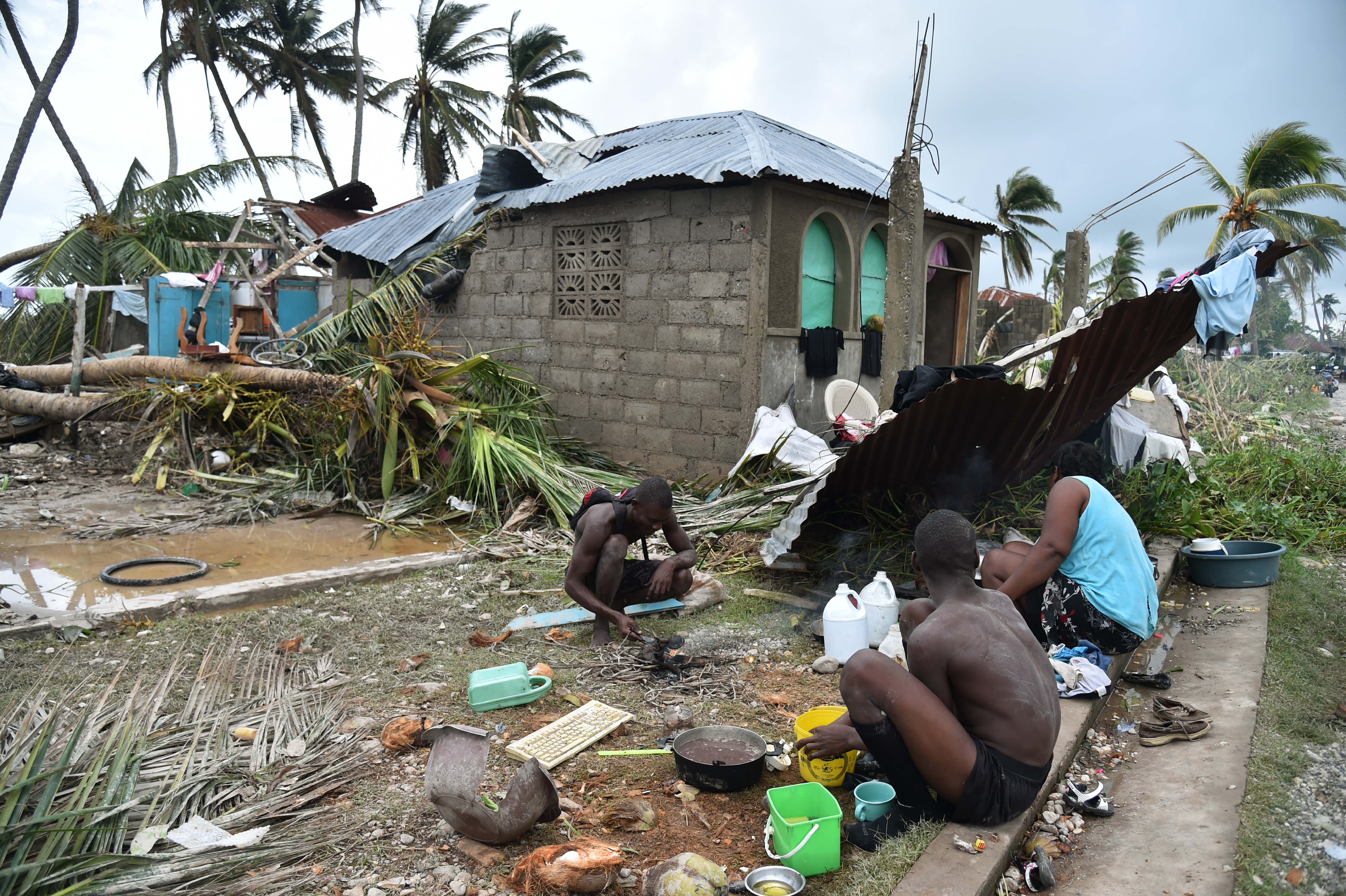 A family prepares food in front of a destroyed house after Hurricane Matthew, in Croix Marche-a-Terre, in Southwest Haiti, on October 6, 2016. The storm killed at least 108 people in Haiti, the poorest country in the Americas, with the final toll expected to be much higher. / AFP PHOTO / HECTOR RETAMAL