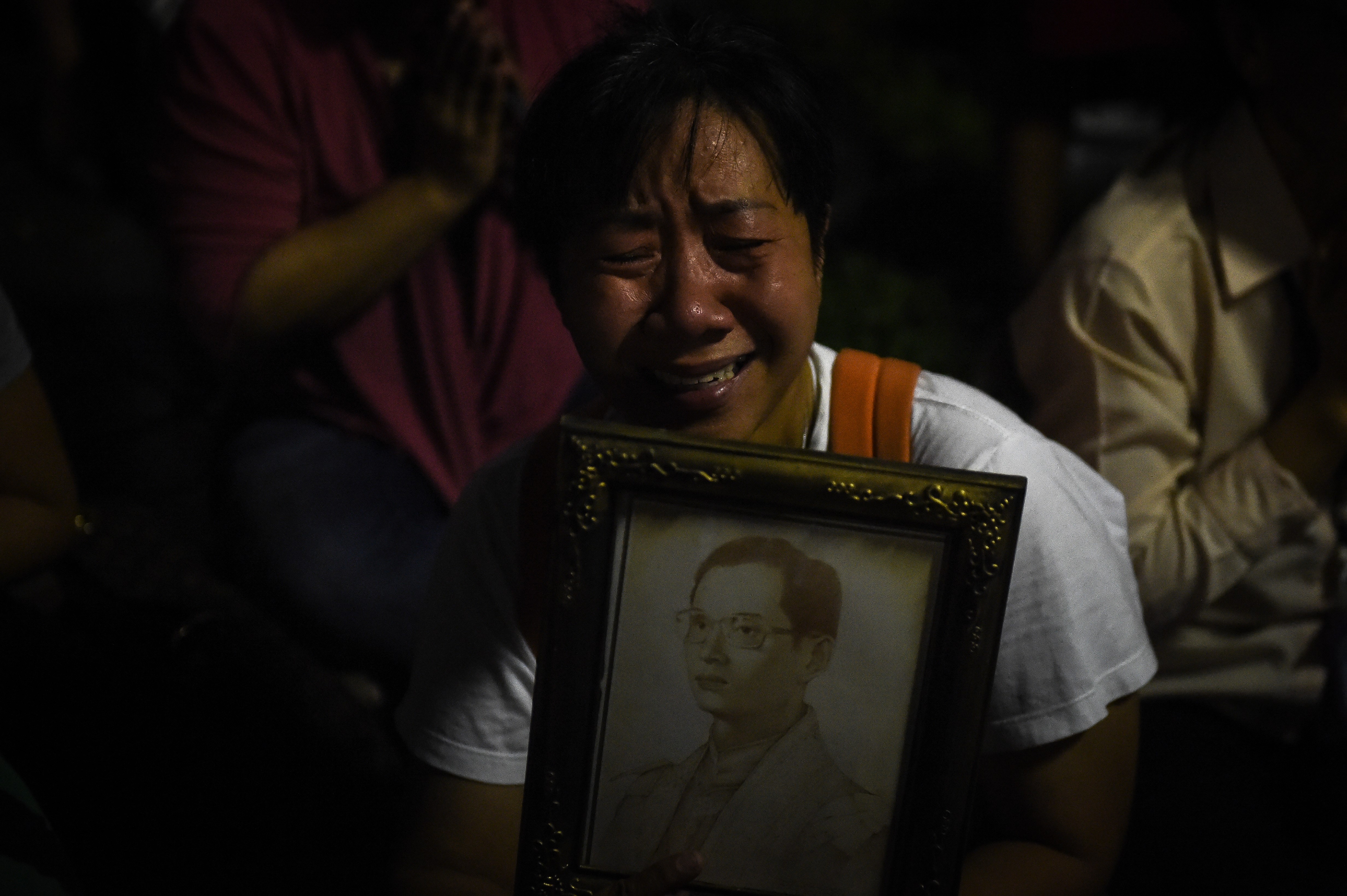 People react to the death of Thailand's King Bhumibol Adulyadej at Siriraj Hospital in Bangkok on October 13, 2016. Thailand's King Bhumibol Adulyadej has died after a long illness, the palace announced on October 13, 2016, ending a remarkable seven-decade reign and leaving a divided people bereft of a towering and rare figure of unity. / AFP PHOTO / LILLIAN SUWANRUMPHA