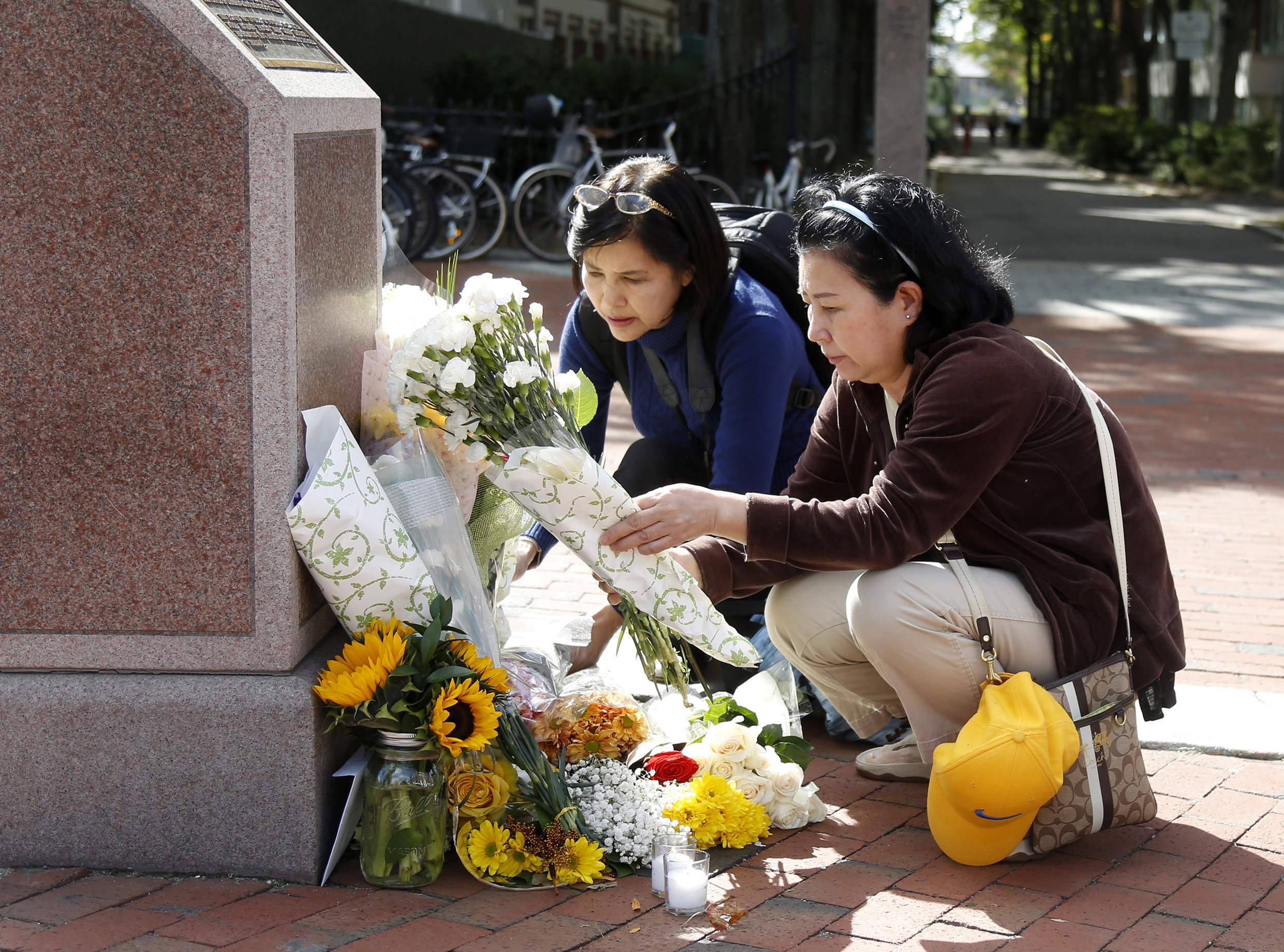 Nayara Amatquanich (C) and Anchulee Astadonwu, both tourists from Thailand, lay flowers and a candle at King Bhumibol Adulyadej Square on October 13, 2016 in Cambridge, Massachusetts. Thailand's King Bhumibol Adulyadej, the world's longest-reigning monarch, has died at the age of 88, the palace announced on October 13, leaving a divided nation bereft of a rare figure of unity. / AFP PHOTO / Mary Schwalm