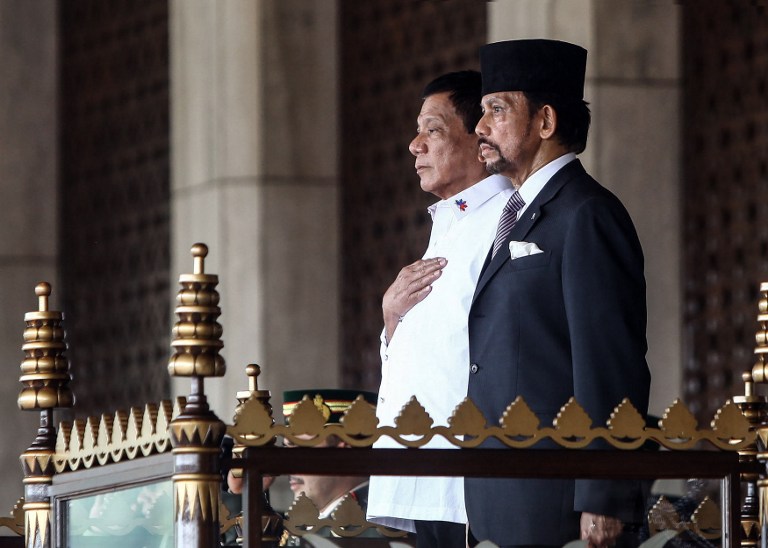 This handout photo released on October 17, 2016 by the Brunei Informations Department shows Brunei's Sultan Hassanal Bolkiah (R) and Philippines' President Rodrigo Duterte standing for national anthems during Duterte's official welcoming ceremony at the Istana Nurul Iman in Brunei. Duterte arrived in Brunei for a three-day official visit and will hold talks with Sultan Bolkiah on bilateral and international issues. / AFP PHOTO / Brunei Informations Department / STR / RESTRICTED TO EDITORIAL USE - MANDATORY CREDIT "AFP PHOTO / BRUNEI INFORMATIONS DEPARTMENT"