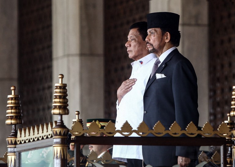 This handout photo released on October 17, 2016 by the Brunei Informations Department shows Brunei's Sultan Hassanal Bolkiah (R) and Philippines' President Rodrigo Duterte  standing for national anthems during Duterte's official welcoming ceremony at the Istana Nurul Iman in Brunei.  Duterte arrived in Brunei for a three-day official visit and will hold talks with Sultan Bolkiah on bilateral and international issues. / AFP PHOTO / Brunei Informations Department / STR / RESTRICTED TO EDITORIAL USE - MANDATORY CREDIT "AFP PHOTO / BRUNEI INFORMATIONS DEPARTMENT" 