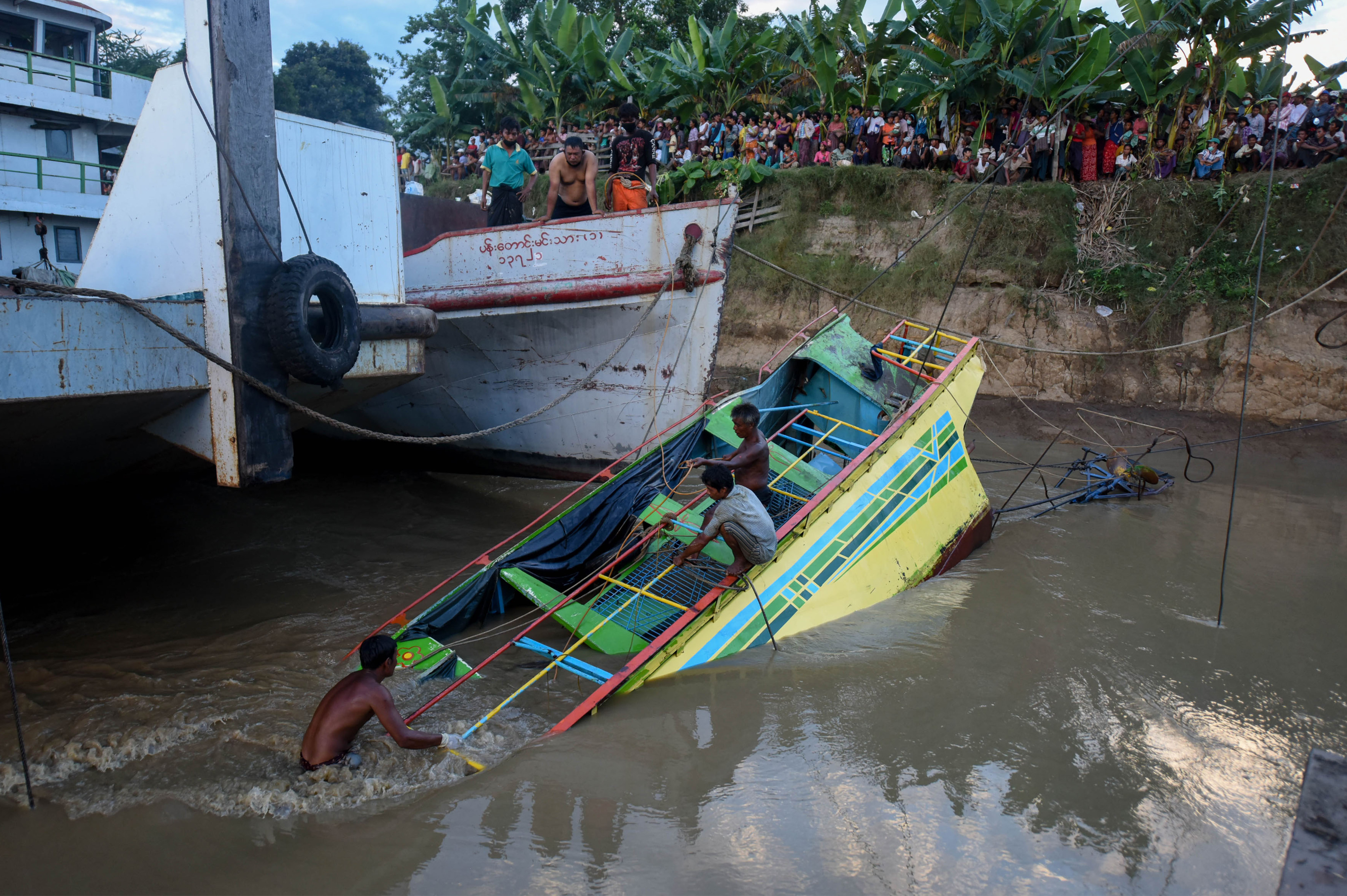 In this photograph taken on October 18, 2016 rescue workers are seen on the sunken ferry partially lifted from the water near the river bank. The death toll from a ferry disaster on a river in central Myanmar four days ago has risen to nearly 50, officials said on October 19, 2016, with most of the deceased identified as women and at least two dozen others still missing. The overloaded vessel, whose passengers included scores of teachers and university students, went down early October 15, 2016 while it was travelling on the Chindwin River in Sagaing region. / AFP PHOTO / STR