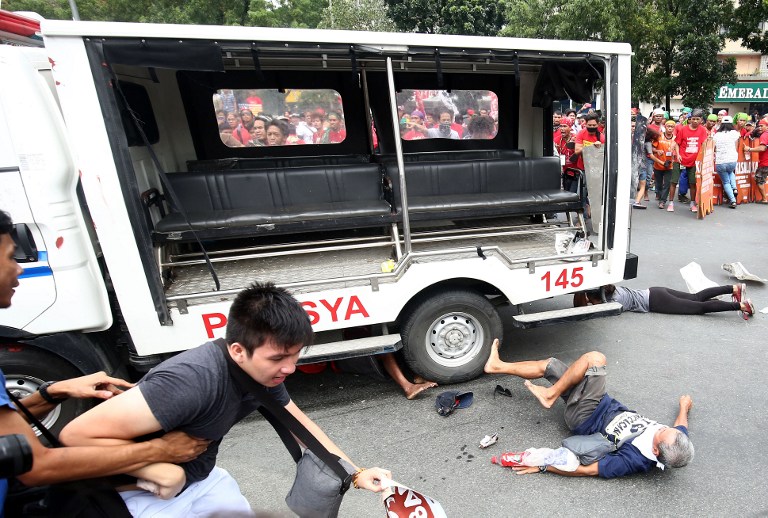 Protesters lie on the ground after being hit by a police van during a rally in front of the US embassy in Manila on October 19, 2016. A Philippine police van on October 19 rammed and ran over baton-wielding protesters outside the US embassy in Manila. / AFP PHOTO / STR