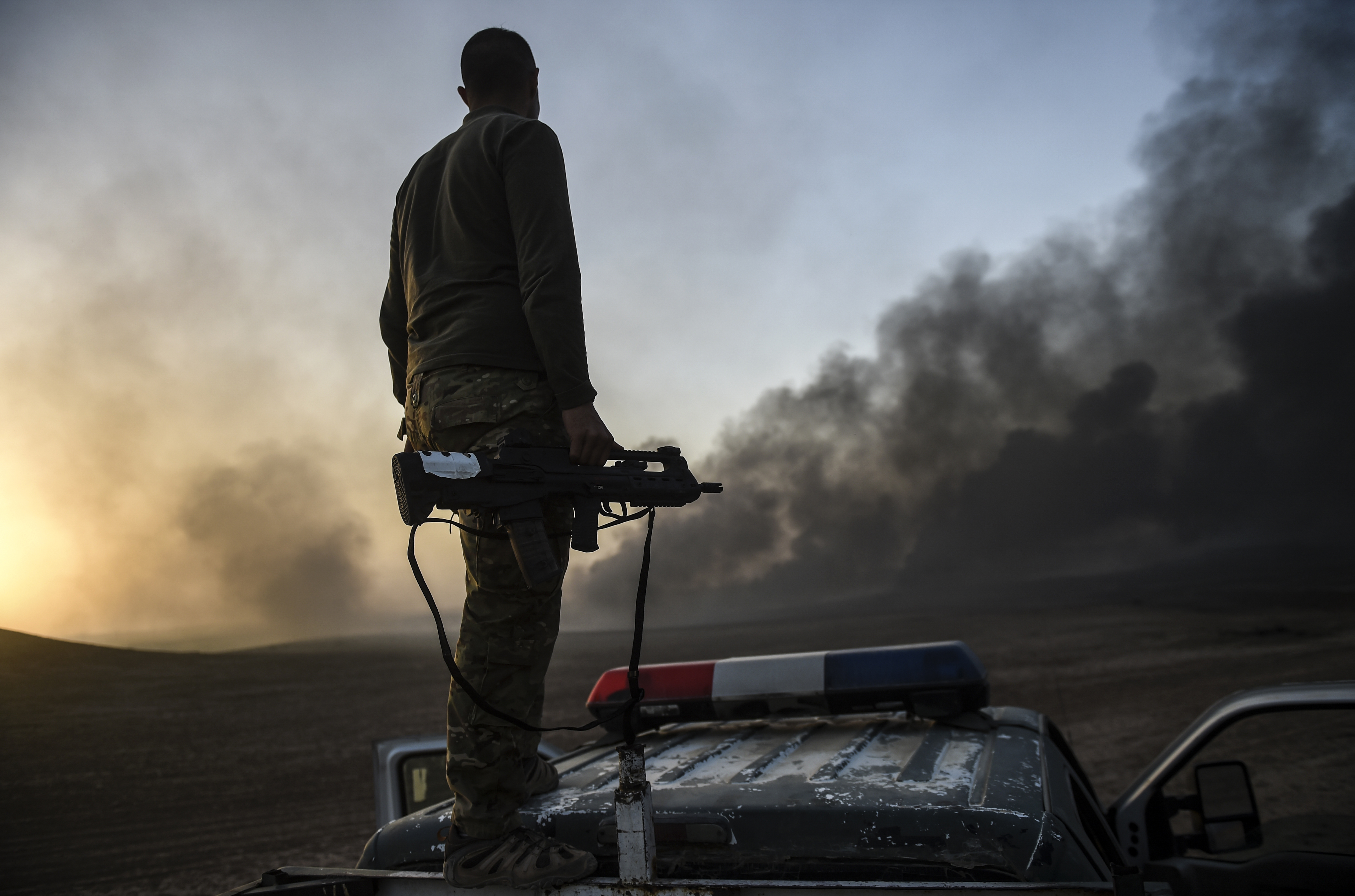 A member of the Iraqi government forces takes a position  on top of a vehicle as smoke rises on the outskirts of the Qayyarah area, some 60 kilometres (35 miles) south of Mosul, on October 20, 2016, during an operation against Islamic State (IS) group jihadists to retake the main hub city. In the biggest Iraqi military operation in years, forces have retaken dozens of villages, mostly south and east of Mosul, and are planning multiple assaults for October 20. / AFP PHOTO / BULENT KILIC