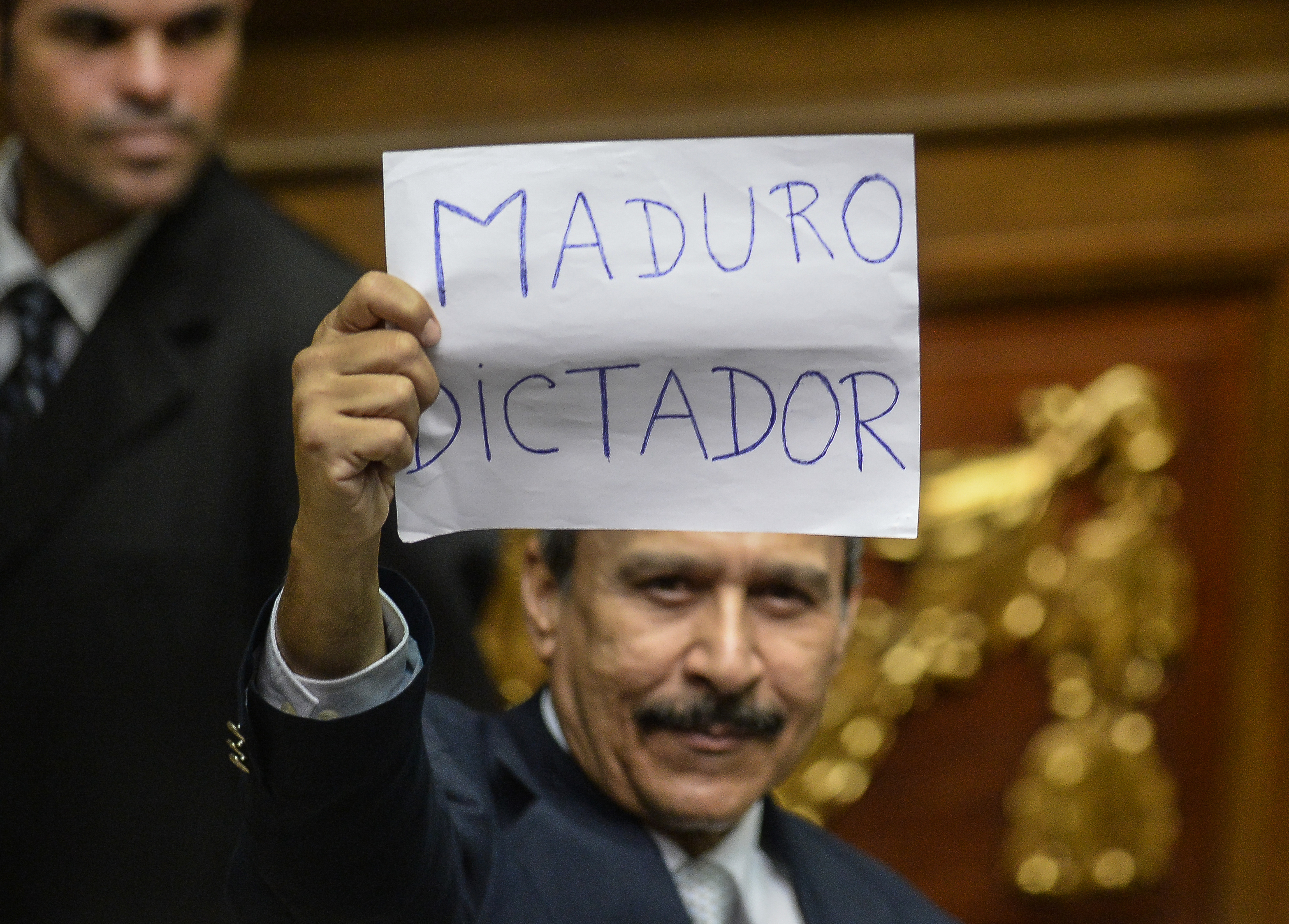 A Venezuelan opposition deputy holds up a sing reading " Maduro dictator"  during an extraoridinary session of the National Assembly, in Caracas on October 23, 2016. Venezuela's opposition-majority legislature declared Sunday that President Nicolas Maduro's "regime" committed a coup d'etat when authorities blocked a referendum on removing the unpopular leftist leader from power. / AFP PHOTO / FEDERICO PARRA